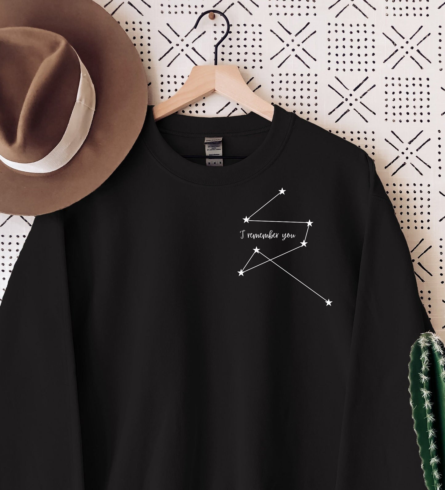 maroon sweatshirt with minimalist white star constellation and the phrase I remember you hanging next to a felt hat and cactus