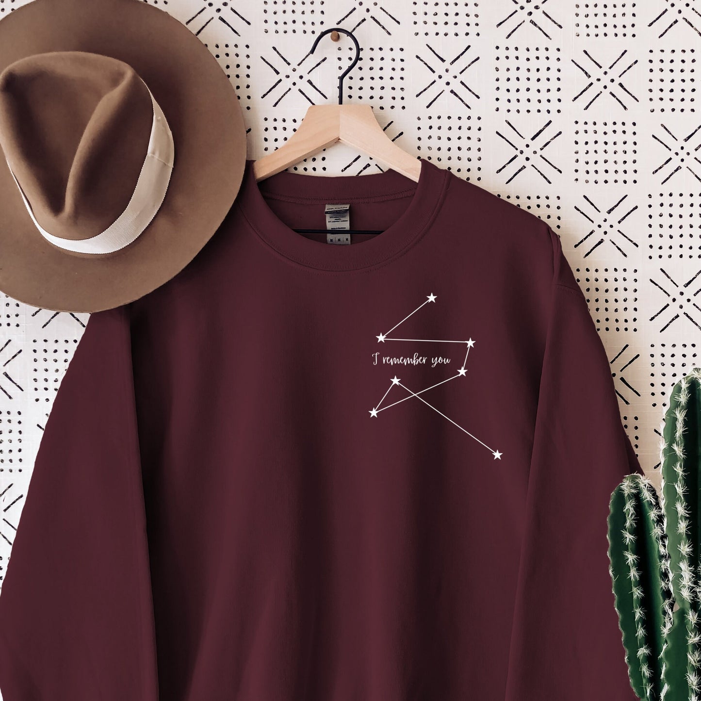 maroon sweatshirt with minimalist white star constellation and the phrase I remember you hanging next to a felt hat and cactus