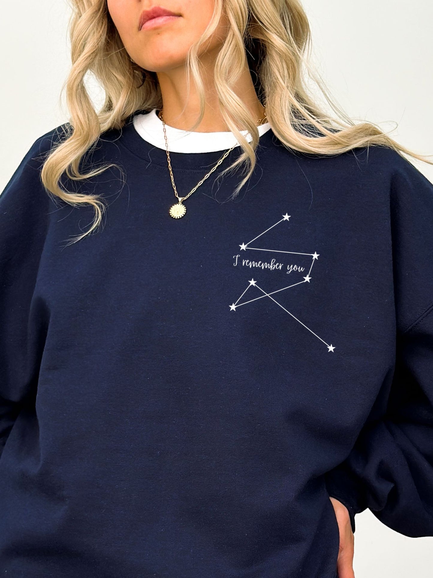 close-up of woman in navy sweatshirt with white celestial star map and I remember you quote near collarbone