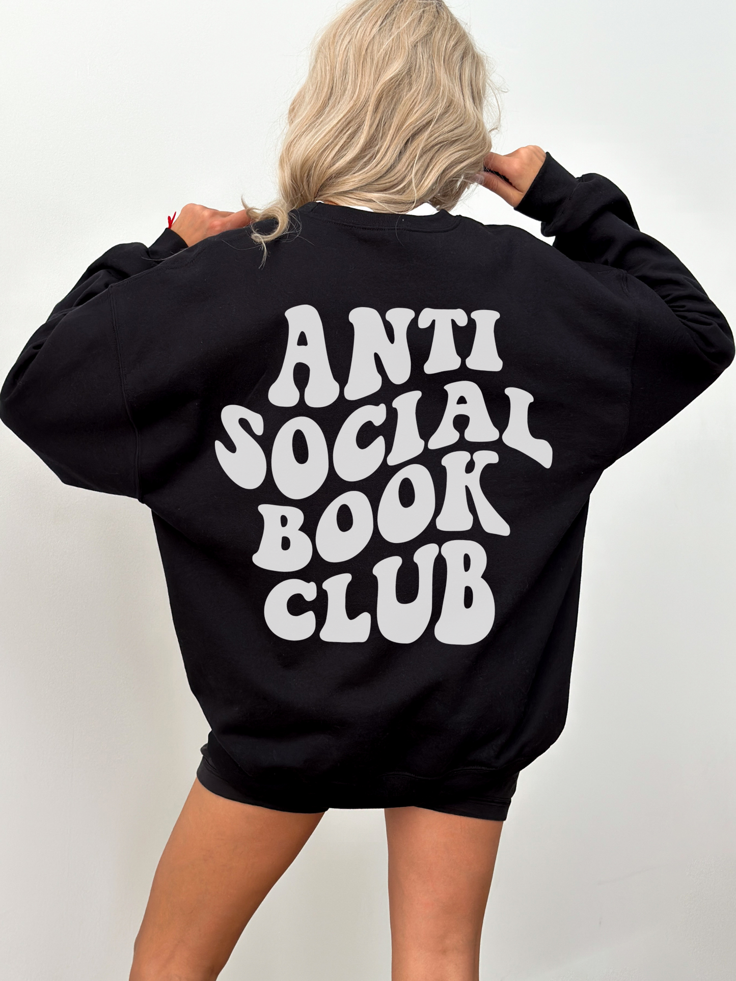 blonde woman facing away wearing oversized black sweatshirt with bold anti social book club text on back