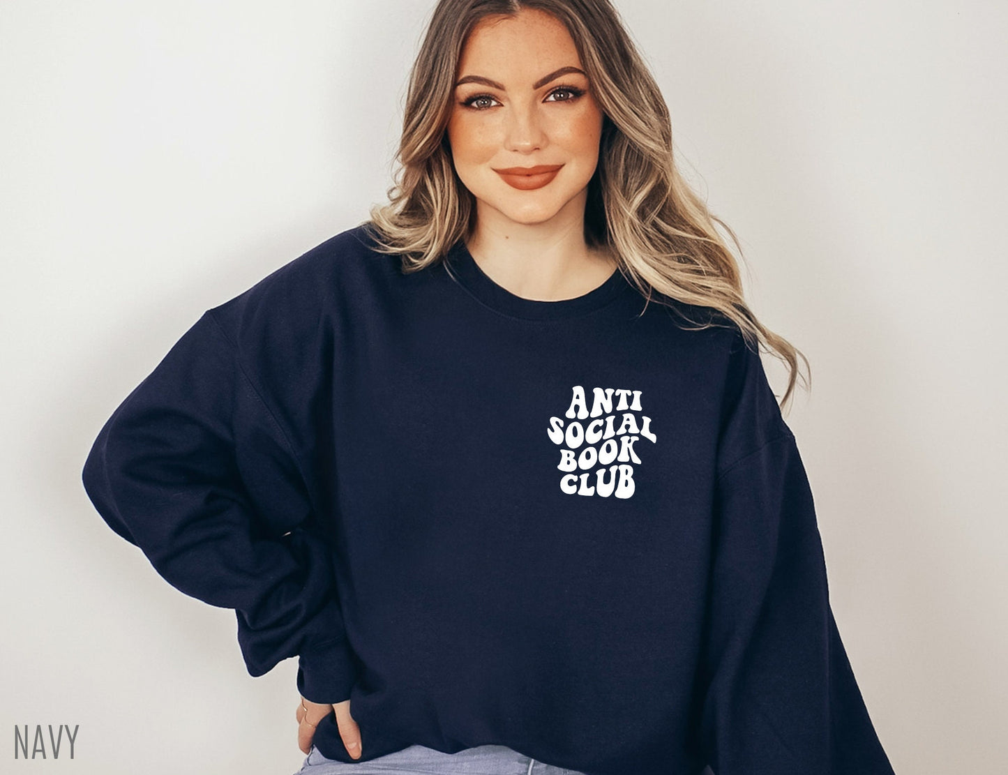 woman wearing navy sweatshirt that says anti social book club standing against neutral wall