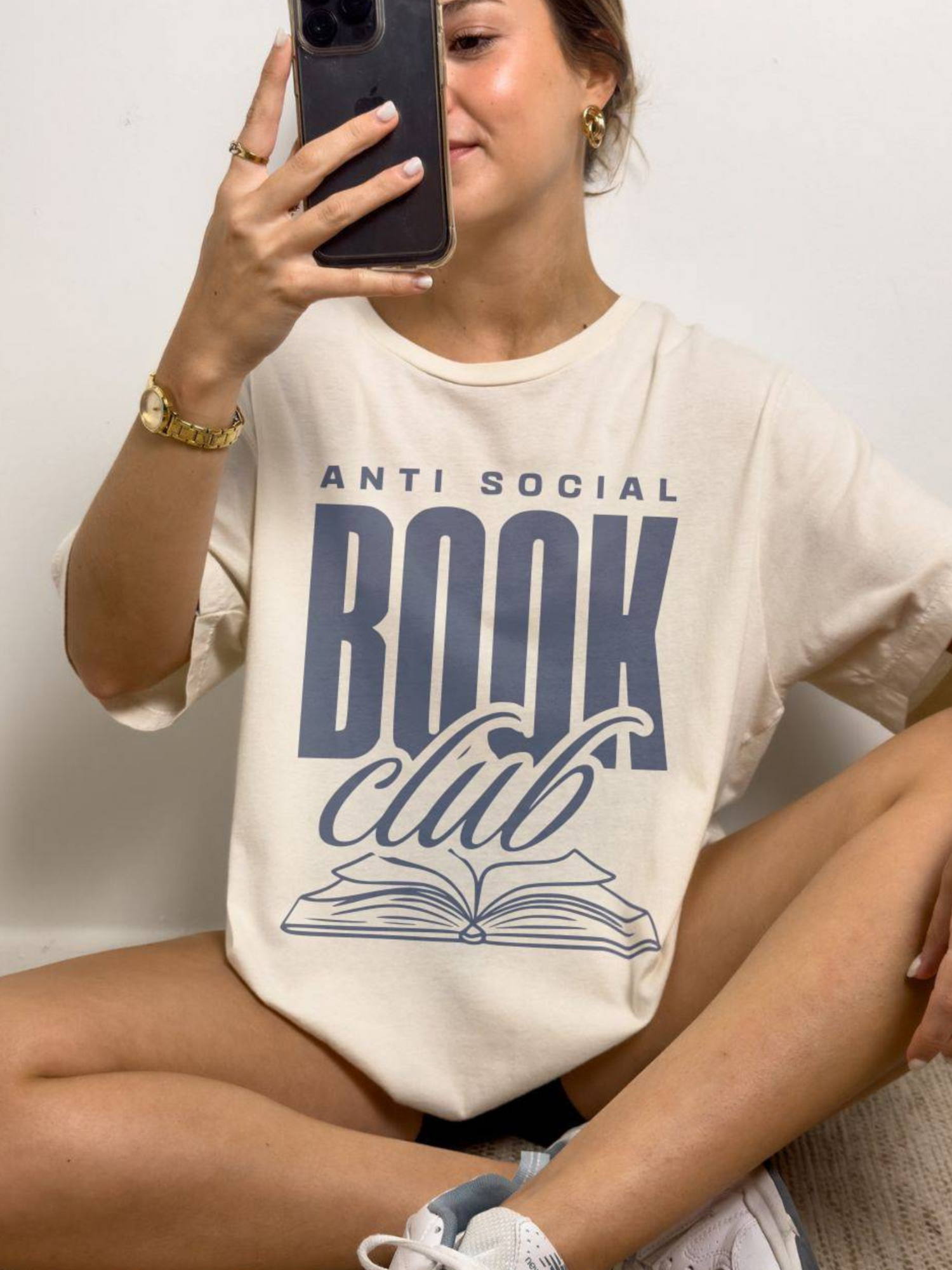 woman taking a selfie in sand-colored anti social book club t-shirt with bold navy font and book illustration