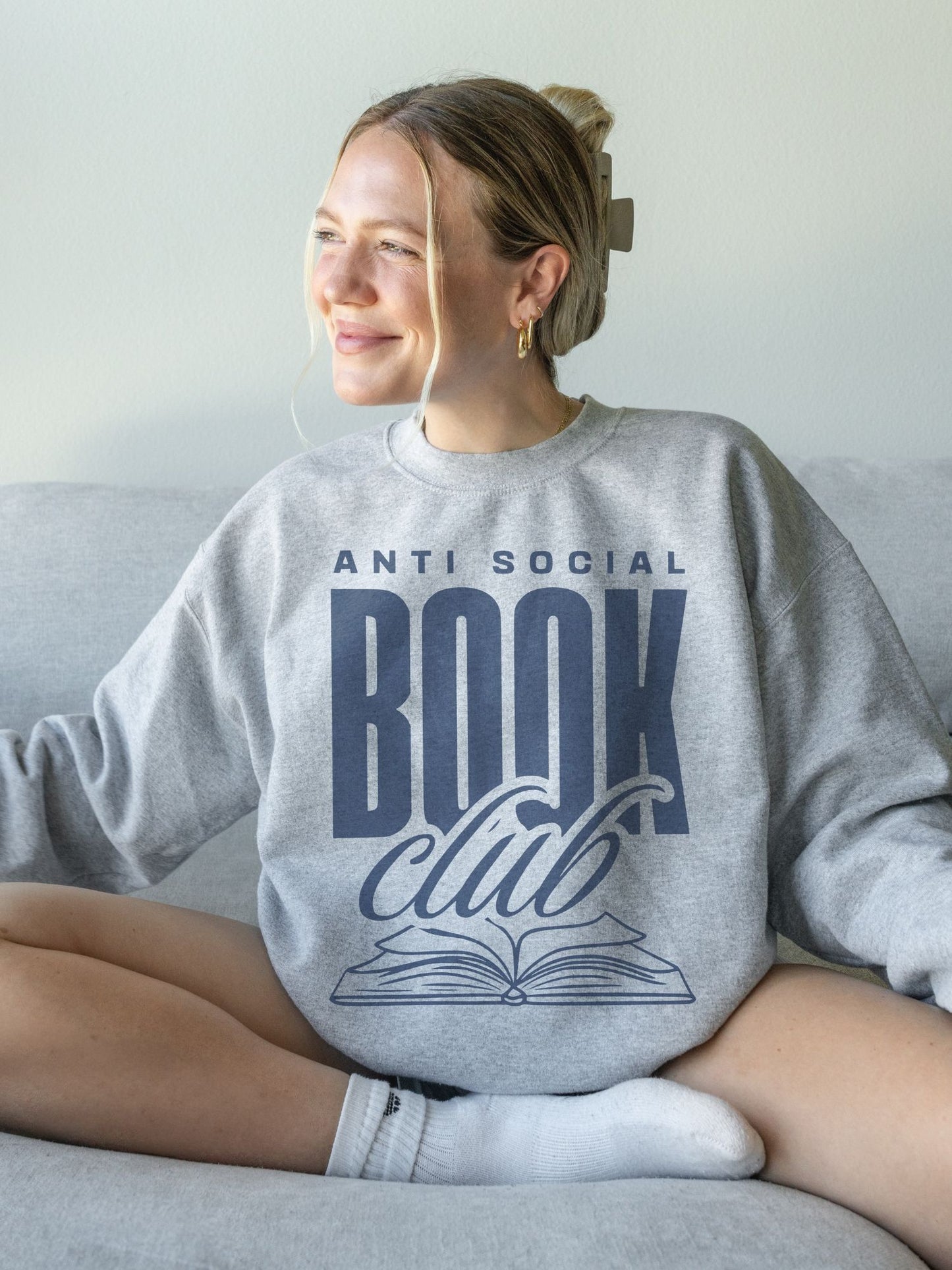 woman sitting on couch wearing ash grey sweatshirt with navy anti social book club text