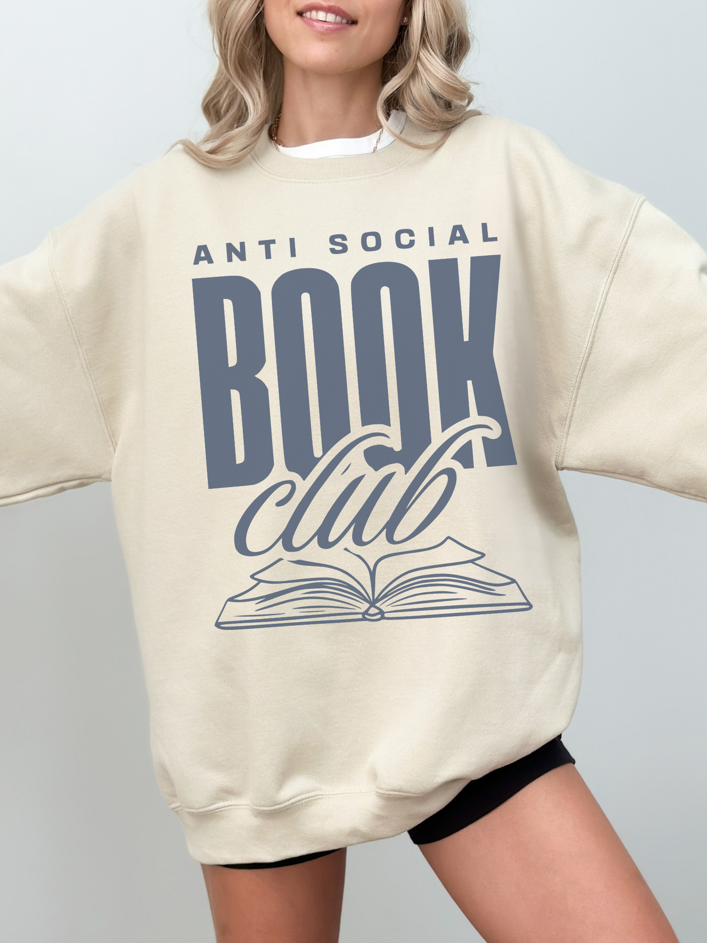 woman wearing oversized sand sweatshirt that says anti social book club with navy font design