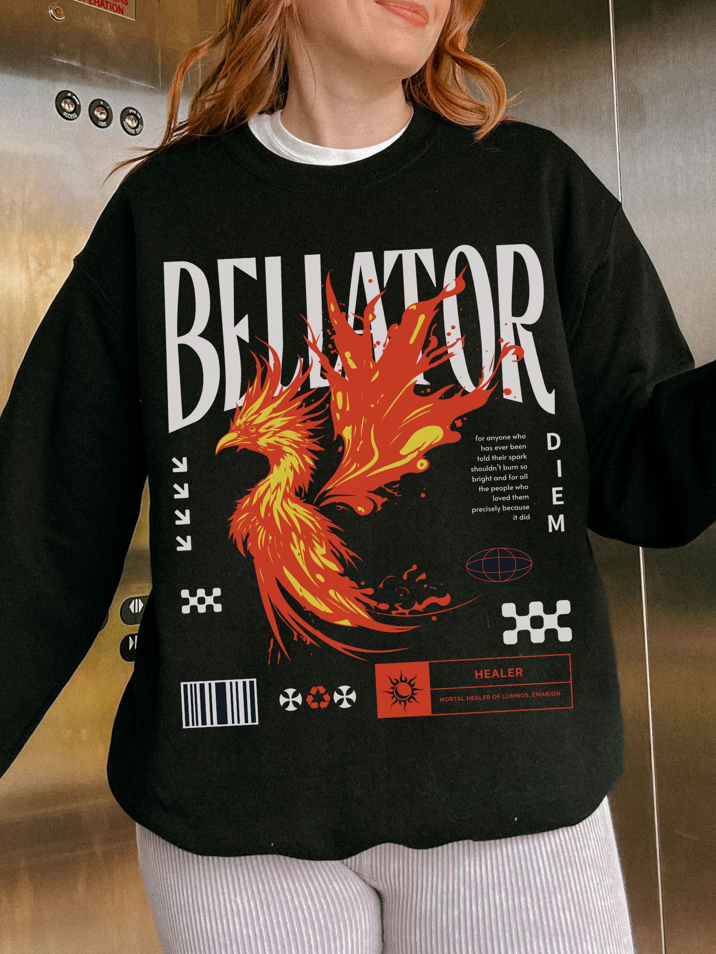 Black phoenix fantasy sweatshirt with Bellator type and healer quote. Worn by redhead model in an elevator with white striped pants and layered tee.