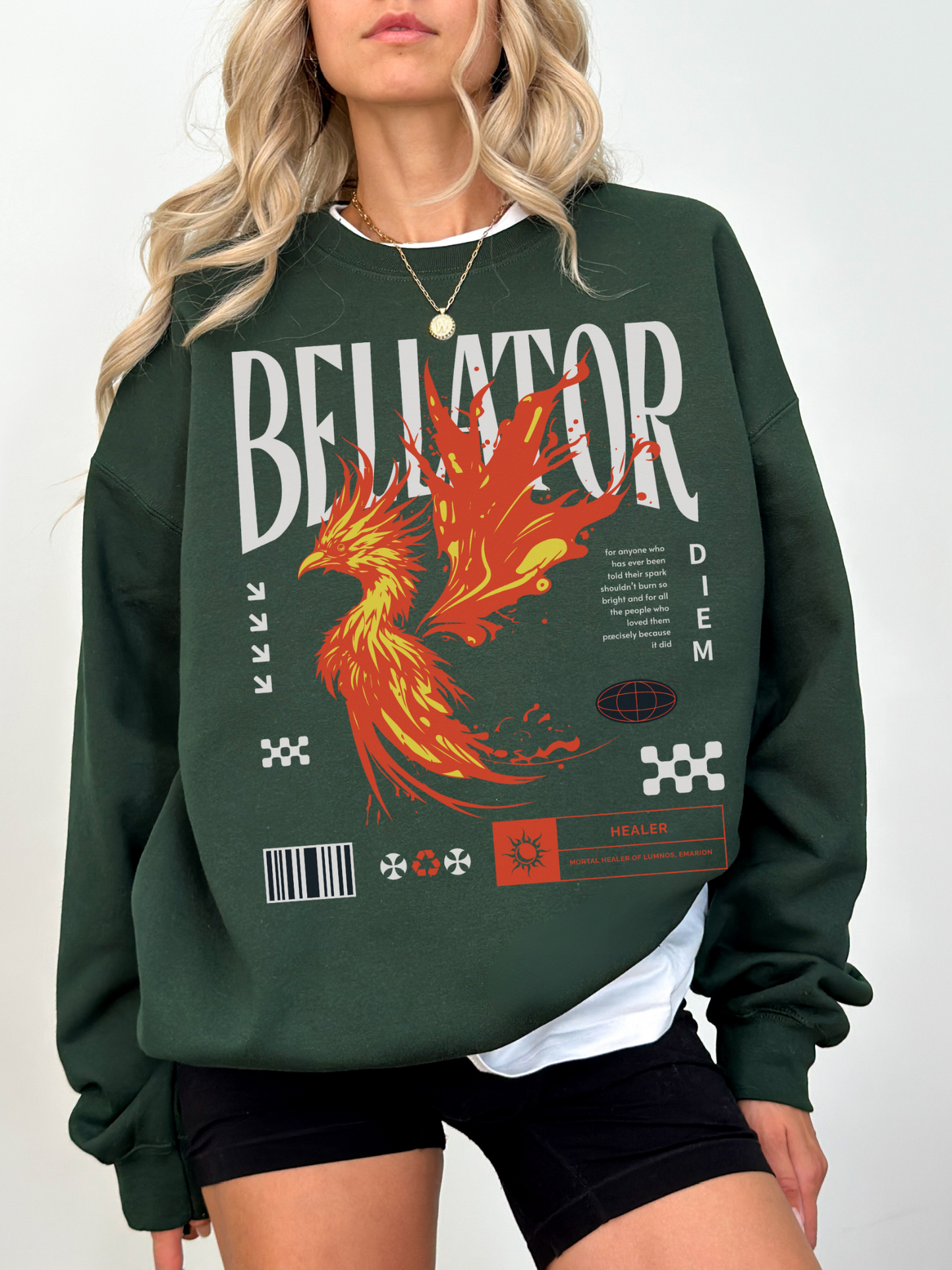 Forest green fantasy sweatshirt with phoenix design and “Bellator” text. Model styled with black shorts and necklace, posed casually for cozy magic-core vibe.