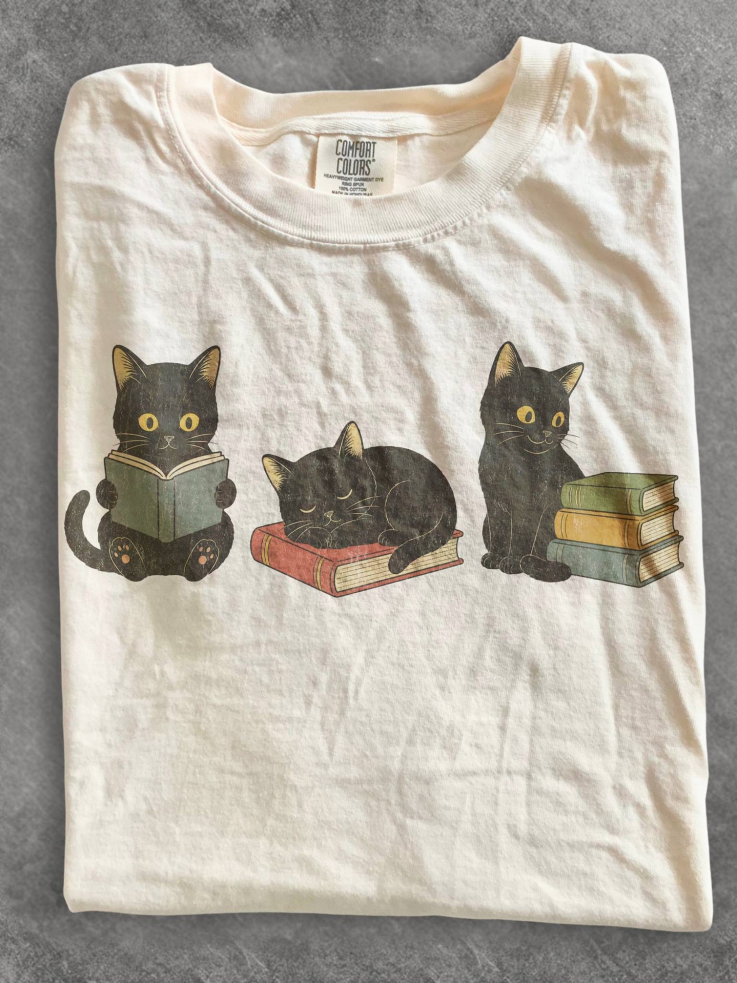 ivory comfort colors t shirt flat lay featuring three black cats with books including a reading cat sleeping cat on a book and cat beside stacked books for book lovers and cat lovers