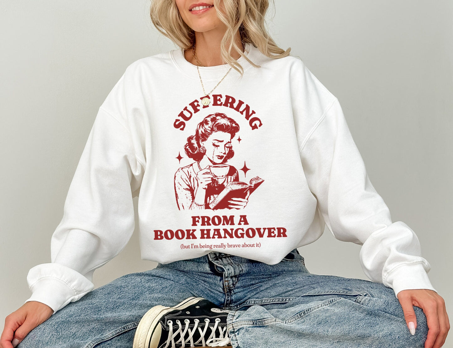 woman in white sweatshirt with red vintage-style book hangover graphic and bold reader quote