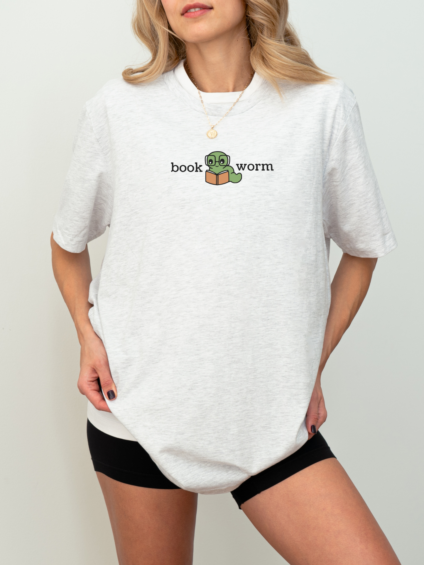 woman wearing an ash grey t-shirt with a centered cartoon worm reading a book and the words book worm