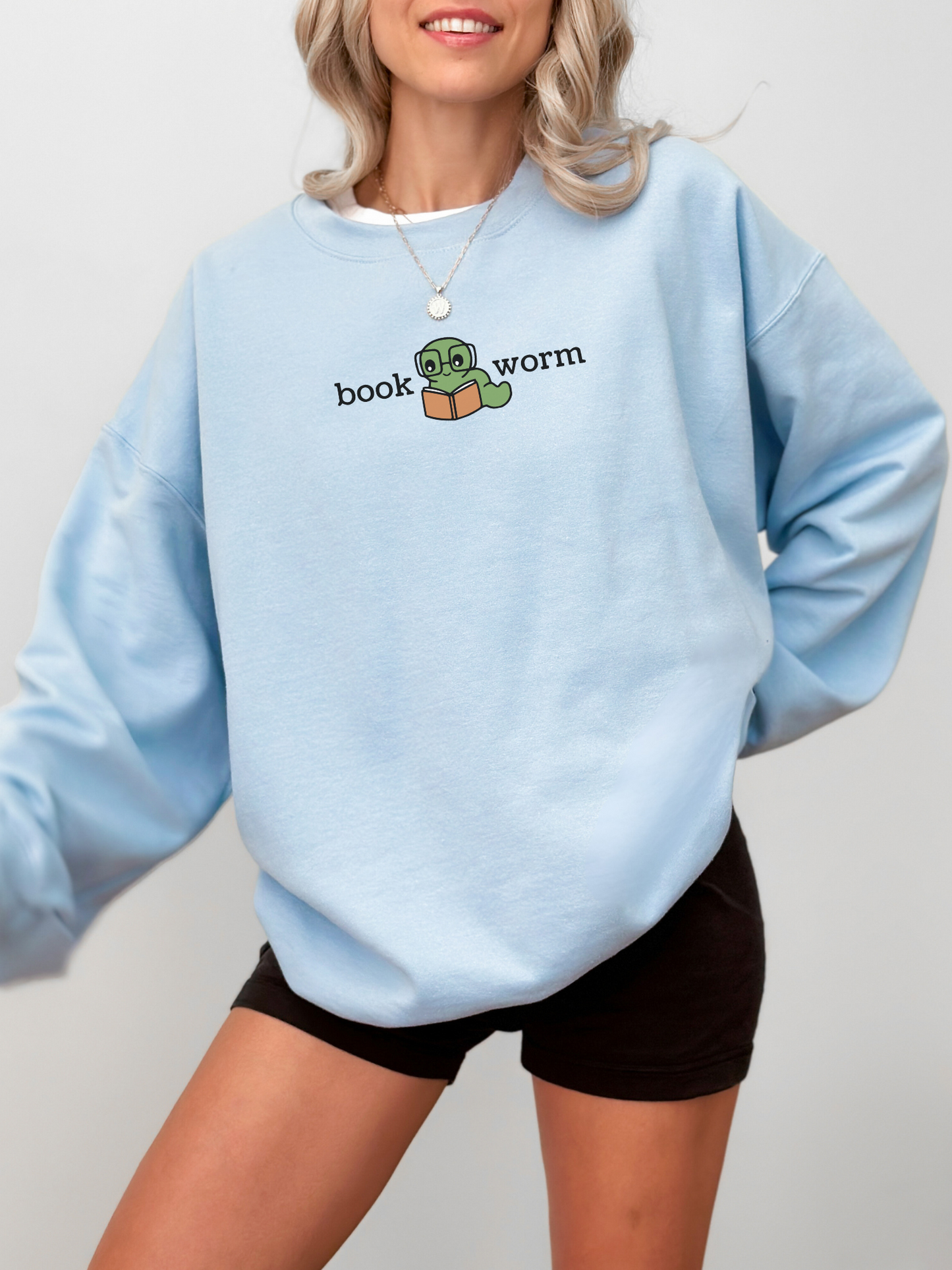 woman wearing a light blue sweatshirt with book worm text and an illustrated green worm with an orange book