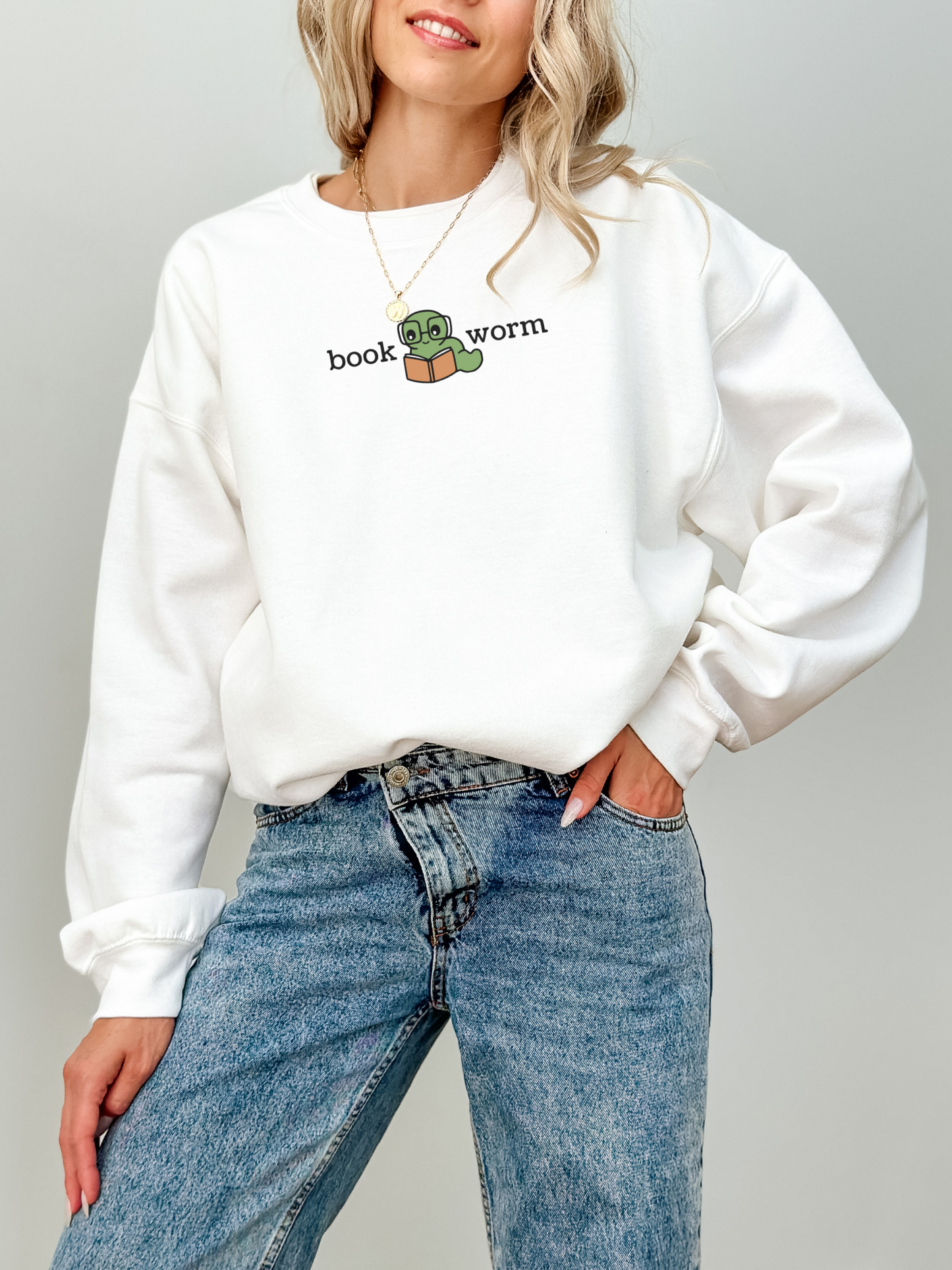 woman wearing a white sweatshirt with a green cartoon worm holding a book and the words book worm in black text