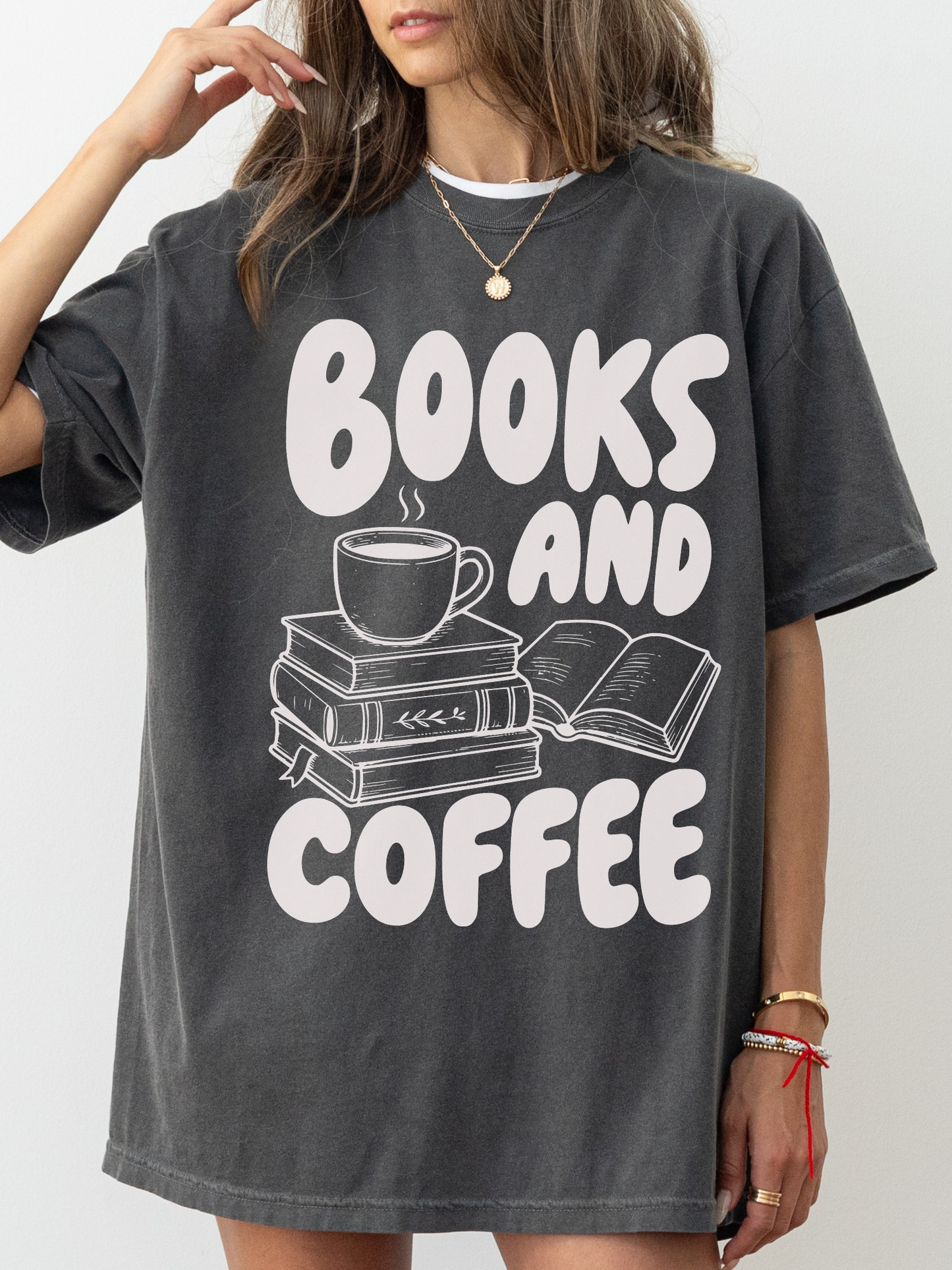 woman wearing a pepper Comfort Colors shirt featuring a books and coffee design with illustrated stacked books, open book, and coffee cup, cozy oversized bookworm shirt for readers and librarians