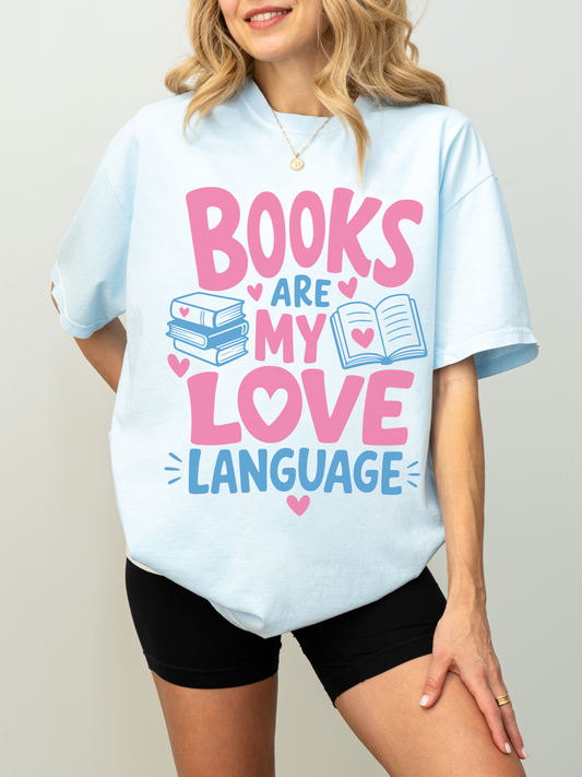 woman wearing a chambray comfort colors t shirt featuring books are my love language graphic with pink and blue lettering book stack open book and heart accents for avid readers