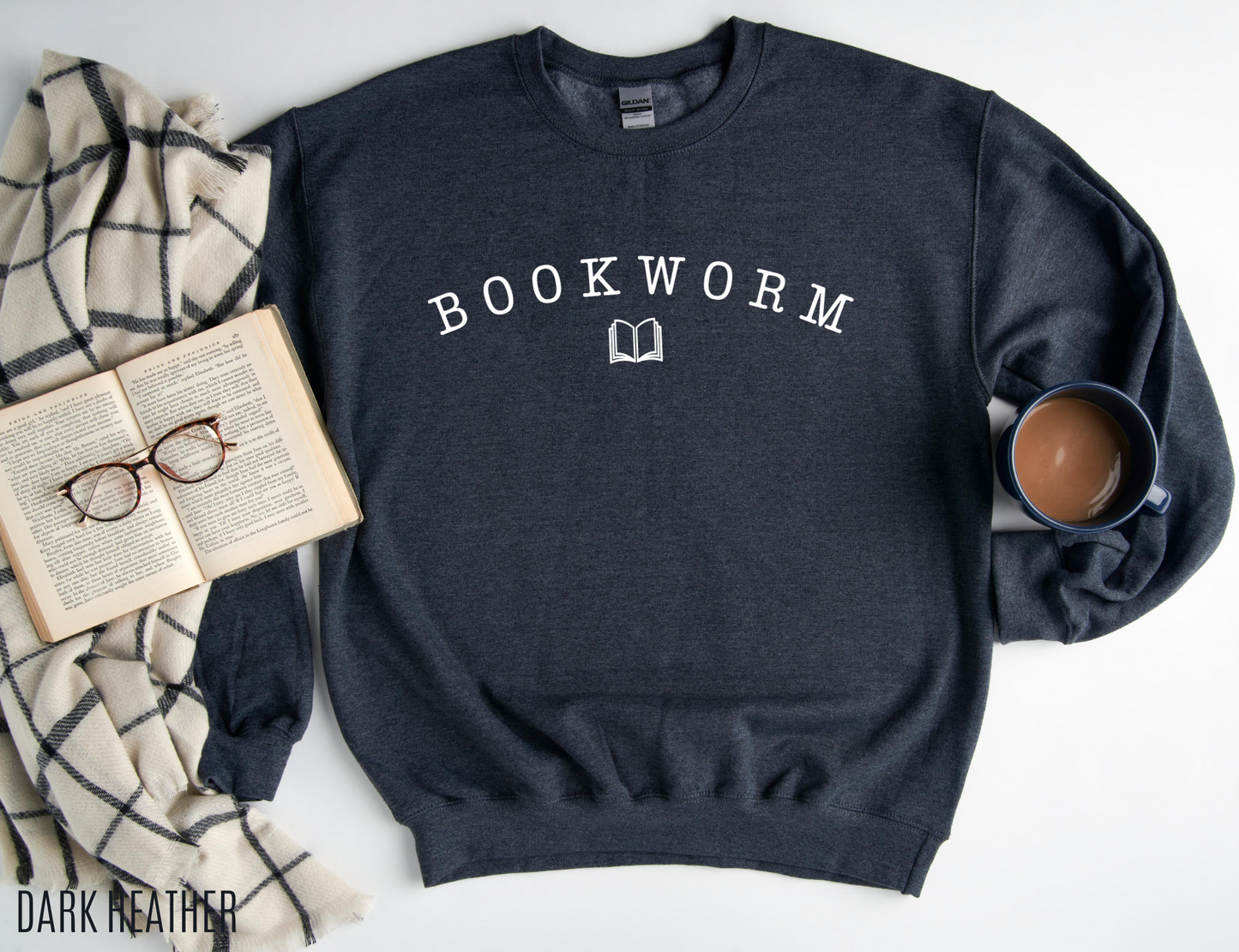 dark heather bookworm sweatshirt styled with open book, plaid blanket, glasses, and mug of coffee for cozy reader vibe