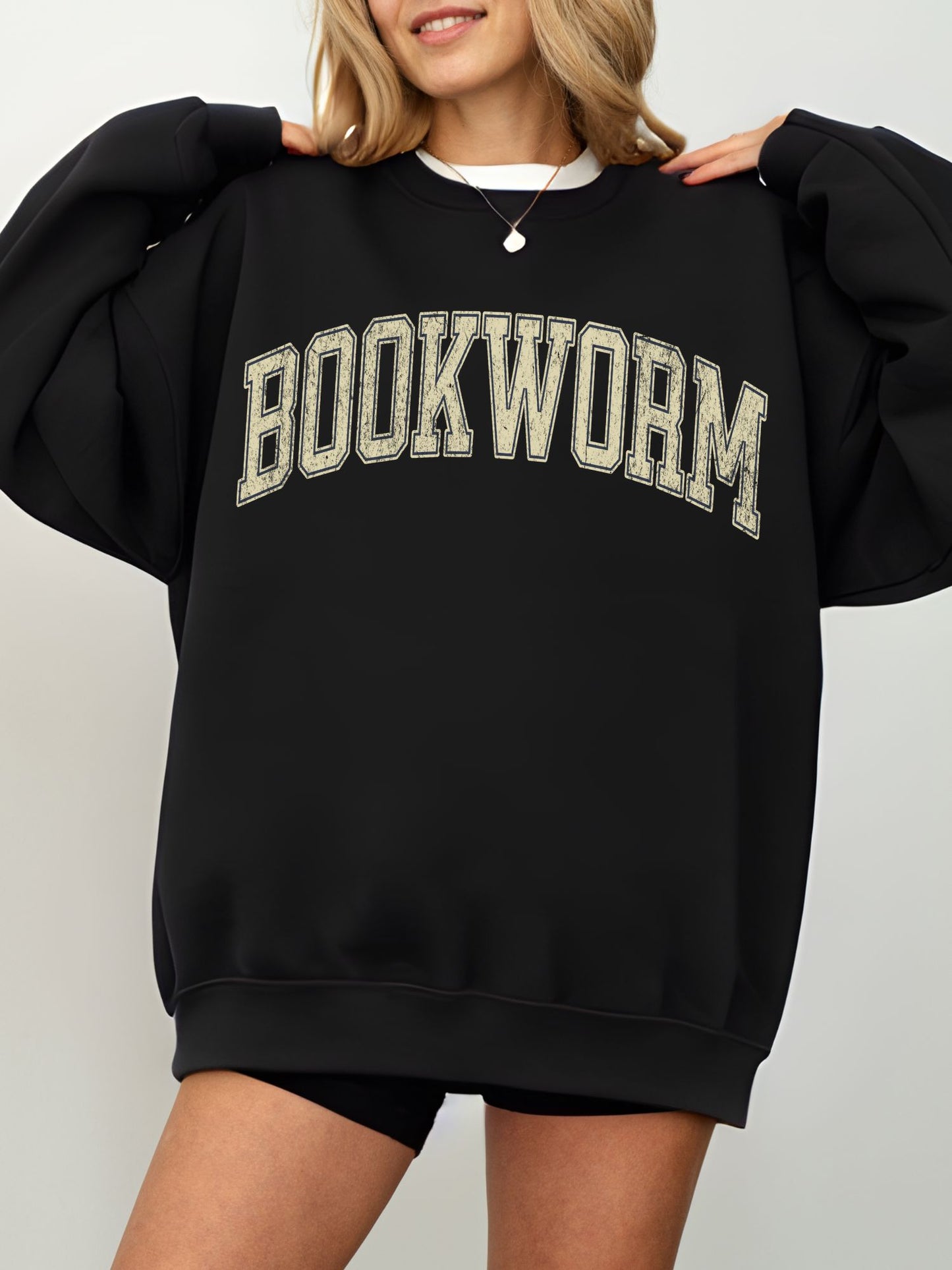 girl standing wearing a black sweatshirt that says "bookworm" across the top in a jersey sport font