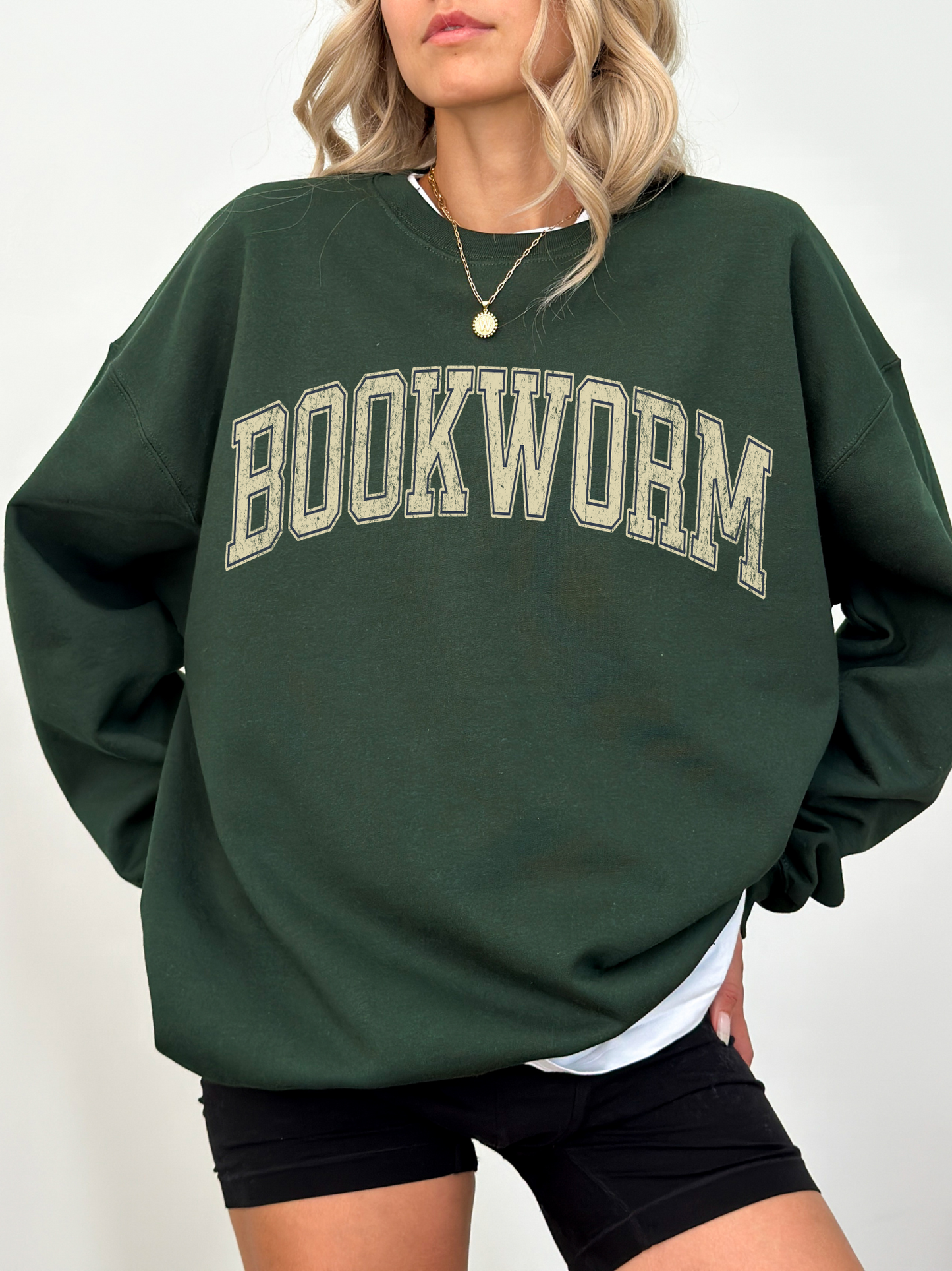 girl standing wearing a forest green sweatshirt that says "bookworm" across the top in a jersey sport font