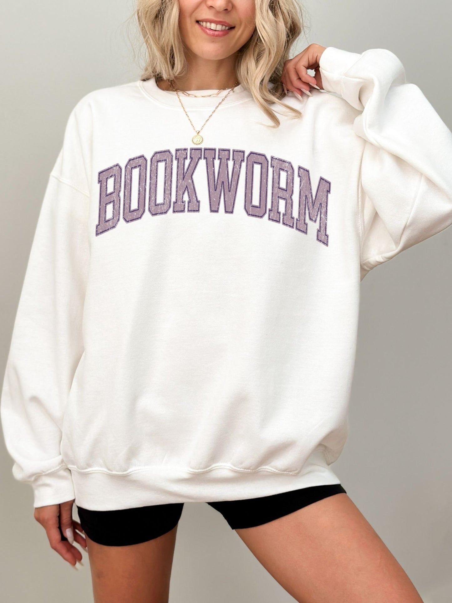 girl standing wearing a white sweatshirt that says "bookworm" across the top in a purple jersey sport font