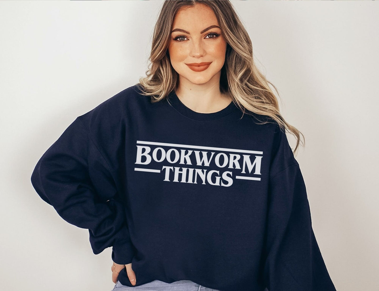 woman wearing navy sweatshirt that says bookworm things in a retro font