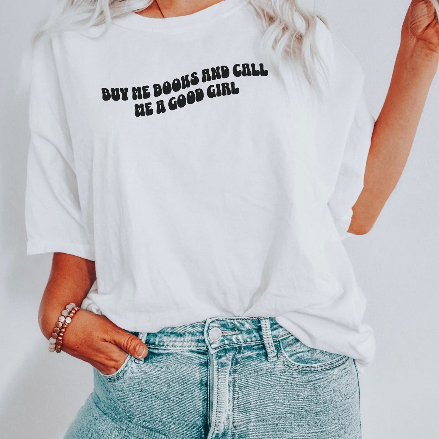 woman wearing white shirt that says buy me books and call me a good girl tucked into light wash jeans