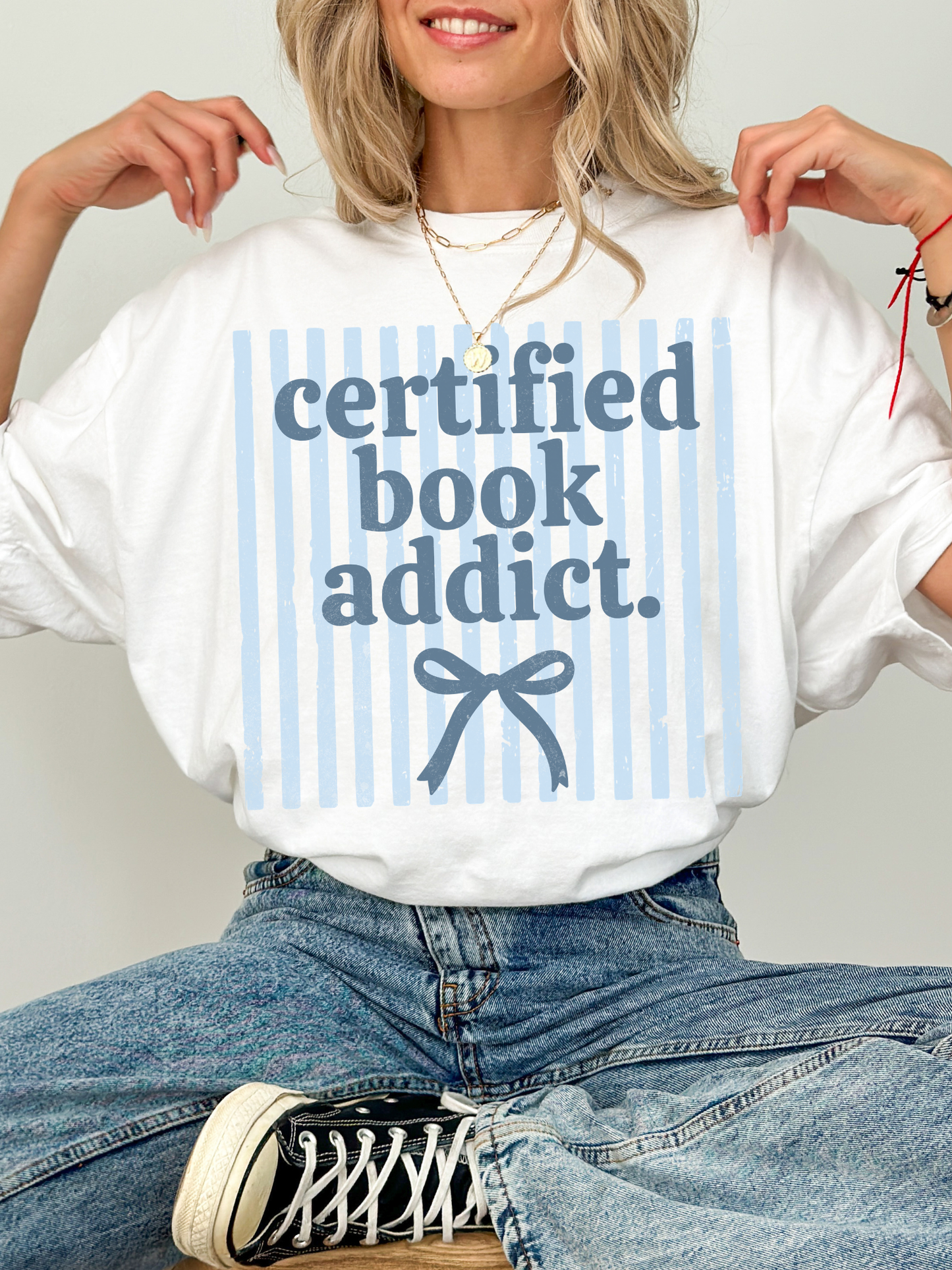 model wearing certified book addict oversized shirt with blue stripe design and bow detail styled with jeans and sneakers