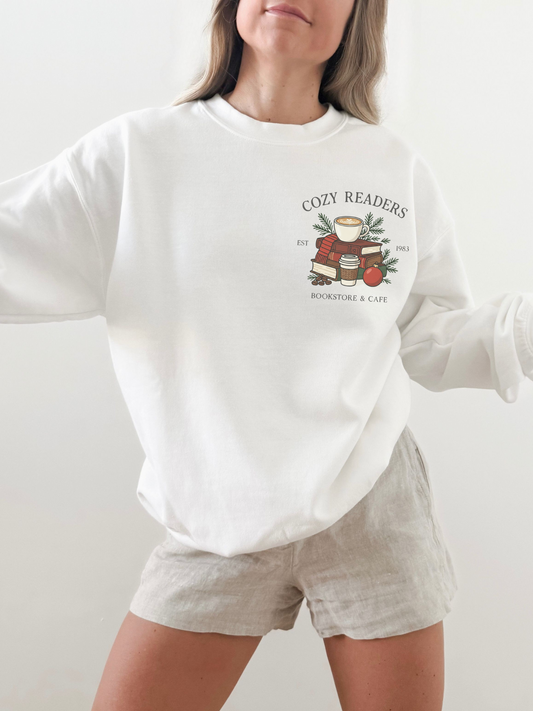 girl standing wearing a white sweatshirt with a small cozy readers coffee shop graphic on the front chest