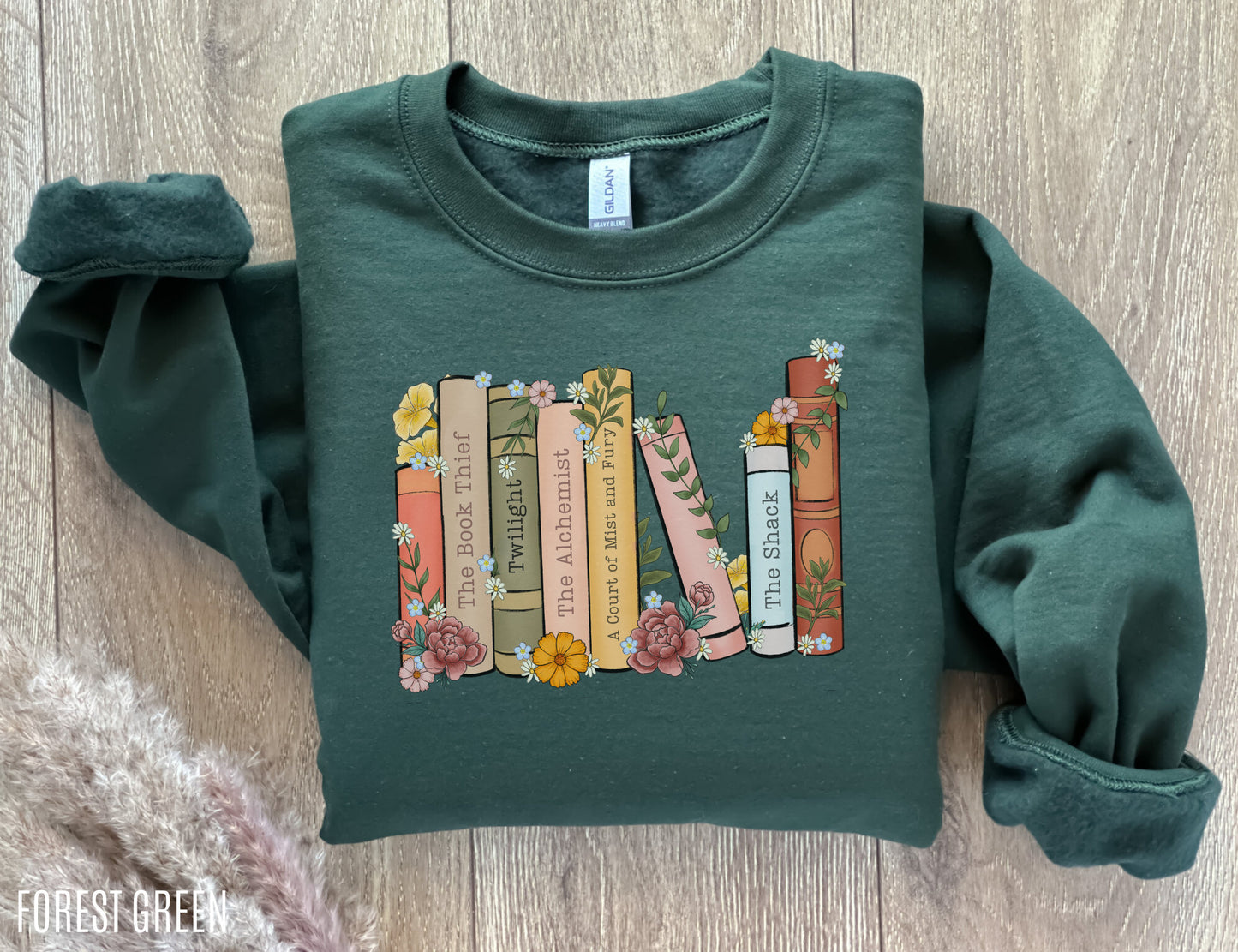 folded forest green sweatshirt with floral illustrated book spines including The Book Thief and A Court of Mist and Fury