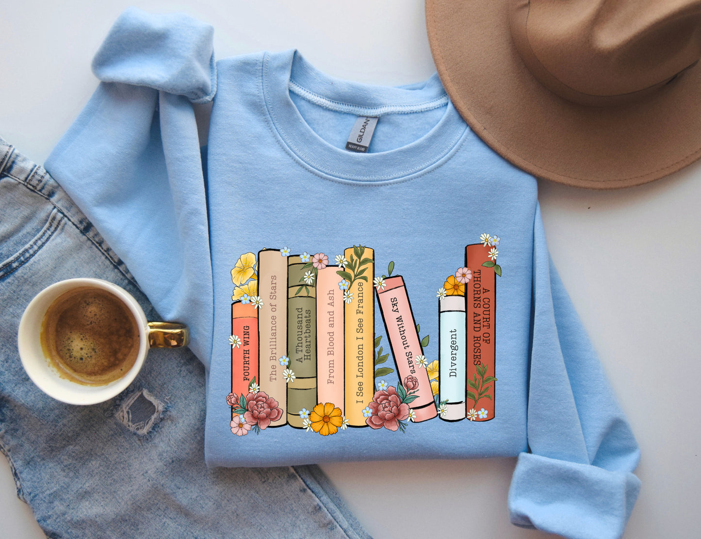 folded light blue sweatshirt with floral bookshelf design featuring Fourth Wing, Divergent, and A Court of Thorns and Roses
