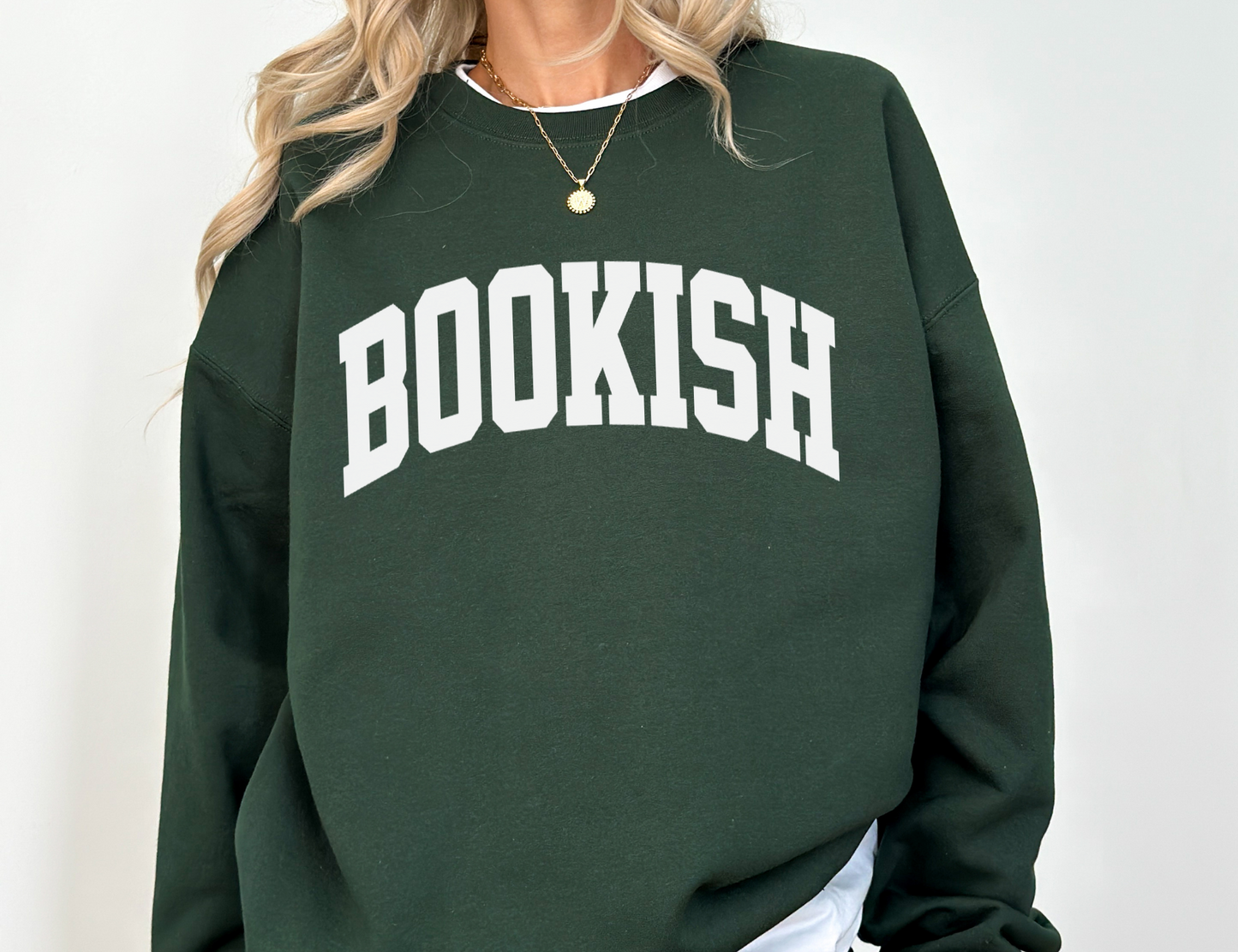 woman wearing forest green sweatshirt with large BOOKISH text, styled casually with layered gold necklace and blonde waves