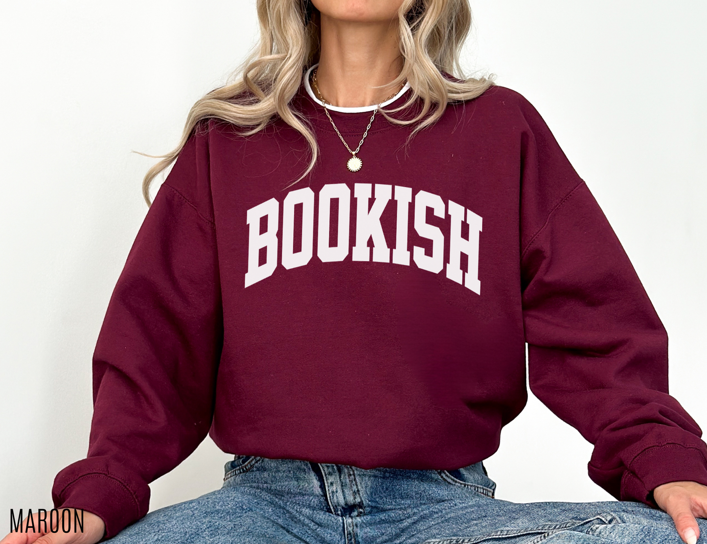maroon BOOKISH sweatshirt worn by woman seated cross-legged in jeans, showing cozy collegiate style