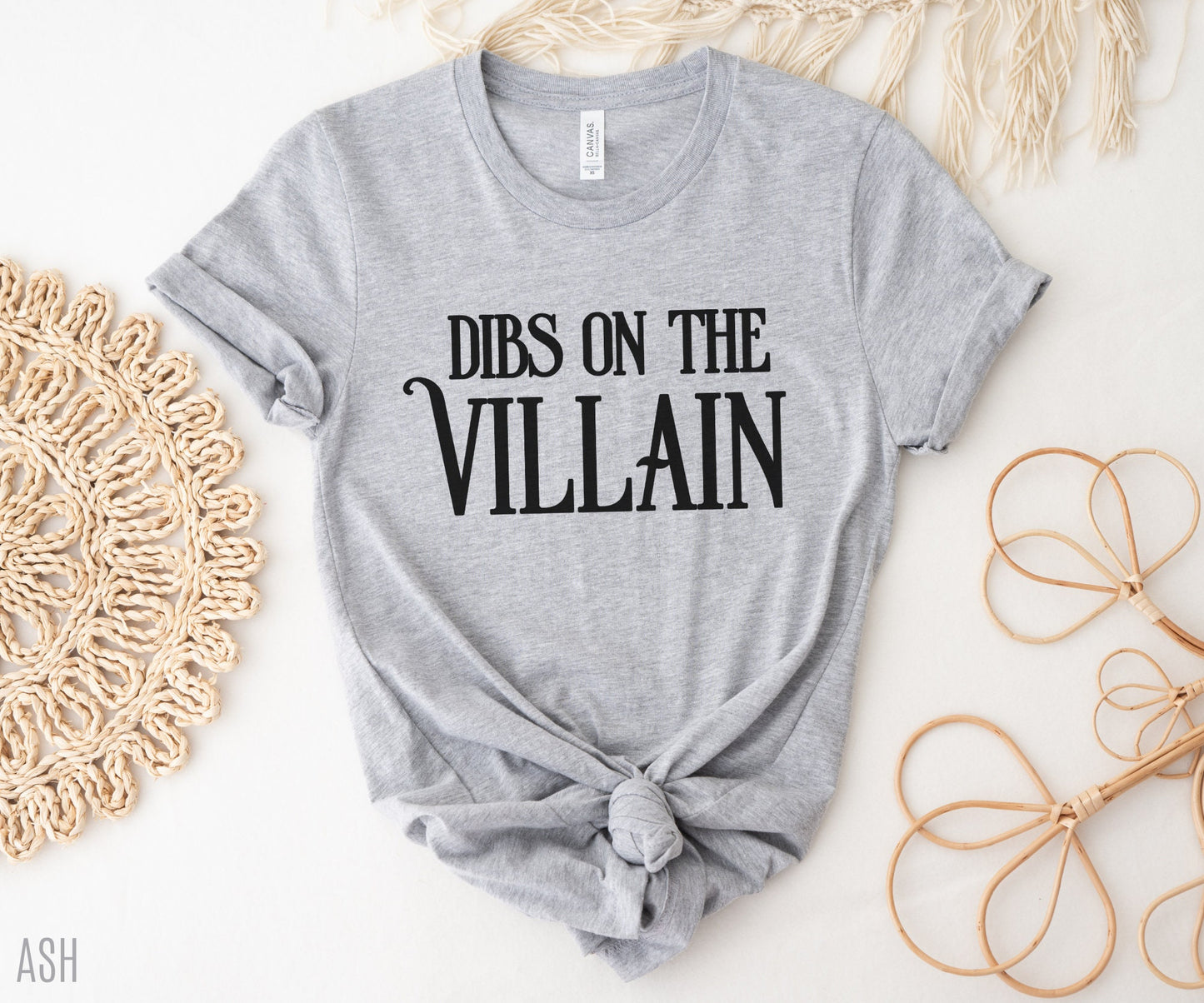 flat lay of ash grey Dibs on the Villain tee with rolled sleeves and neutral boho props