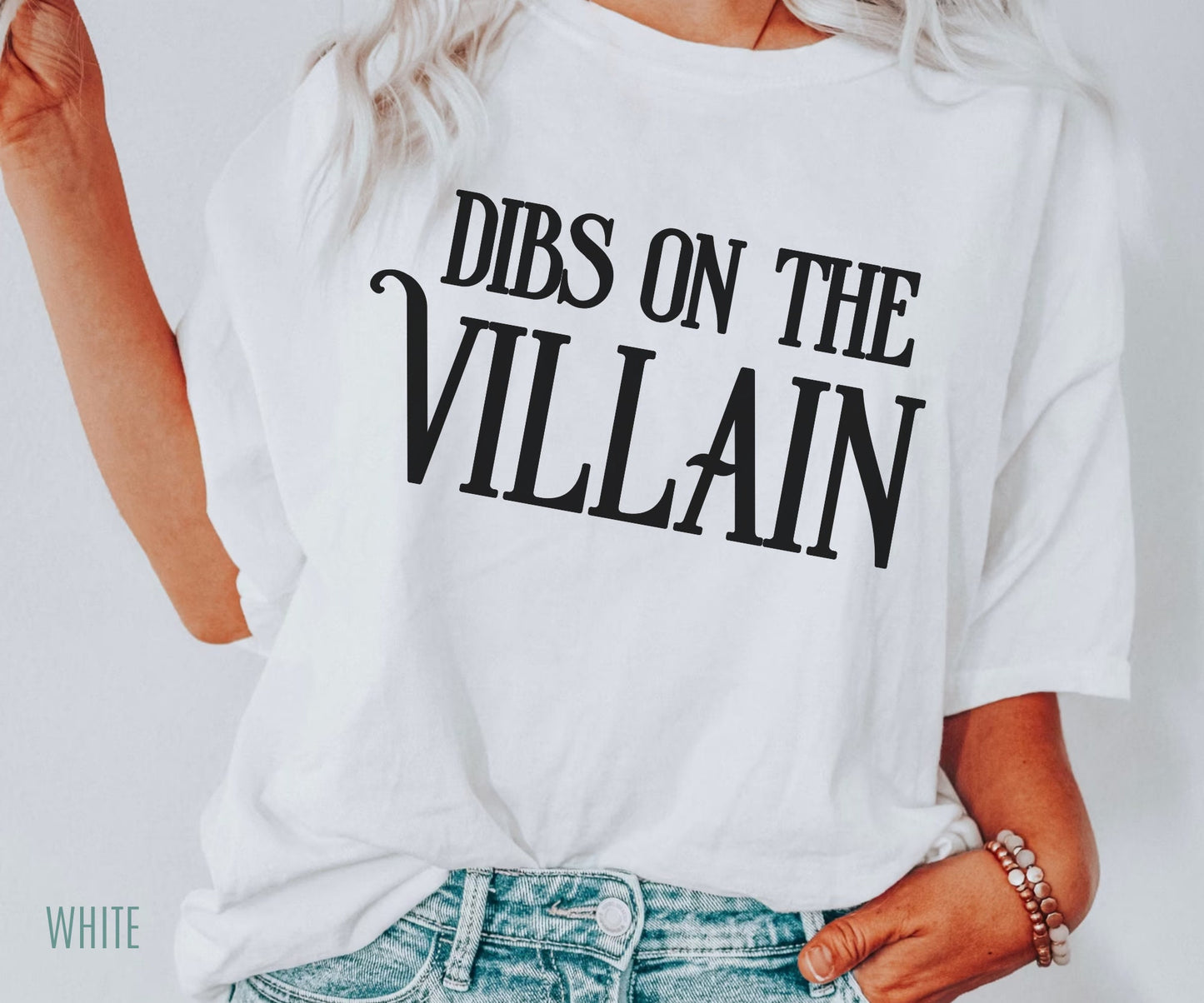 woman wearing oversized white Dibs on the Villain t-shirt with black text, styled with denim