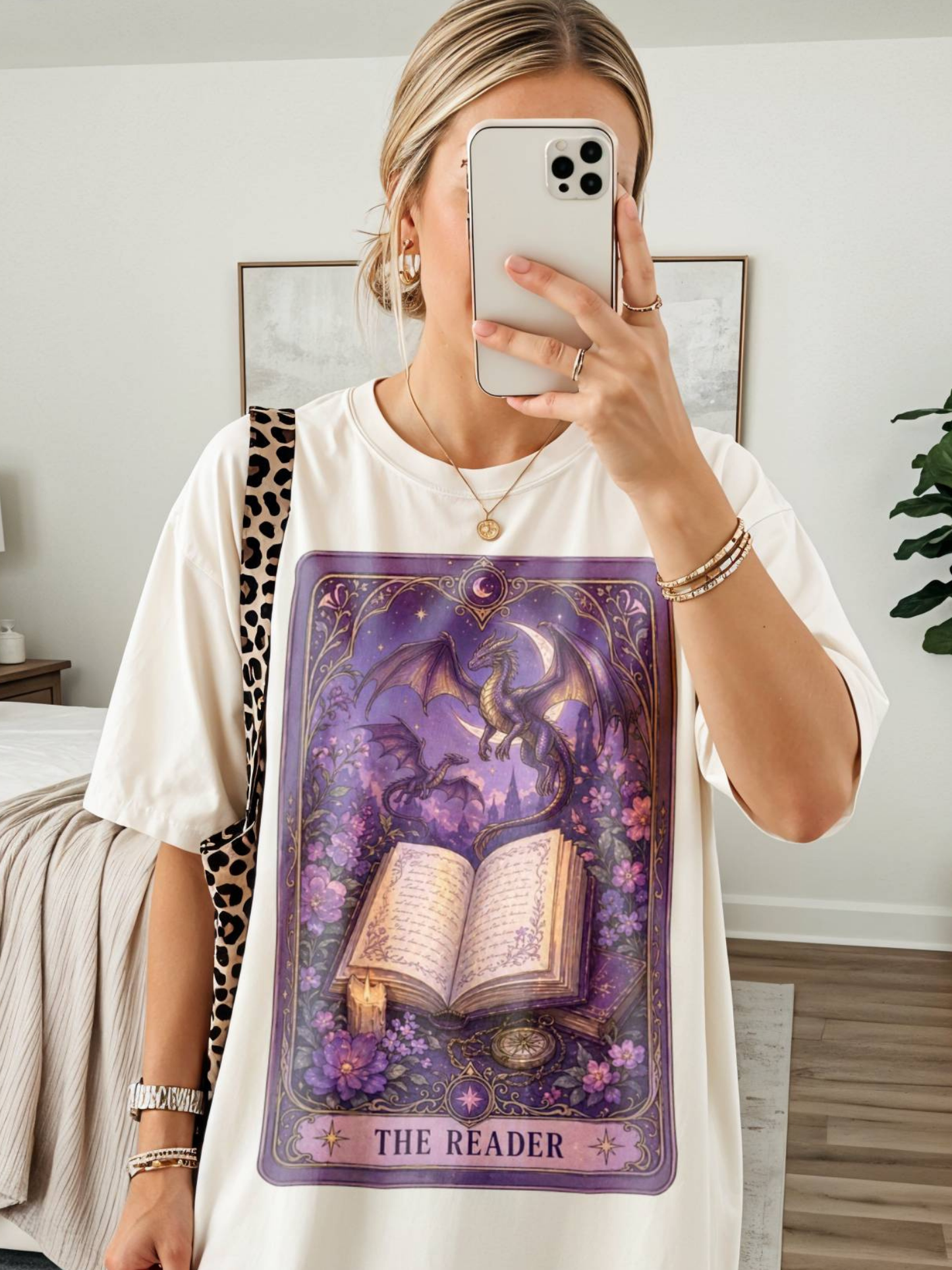 Woman taking mirror selfie wearing cream t shirt with fantasy dragon and open book tarot style artwork labeled the reader purple mystical book lover design