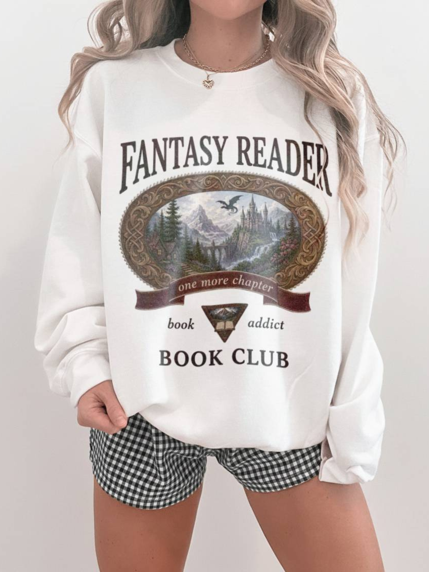 woman wearing a white Fantasy Reader Book Club sweatshirt featuring a fantasy castle, dragon, mountains, and one more chapter design for fantasy book lovers