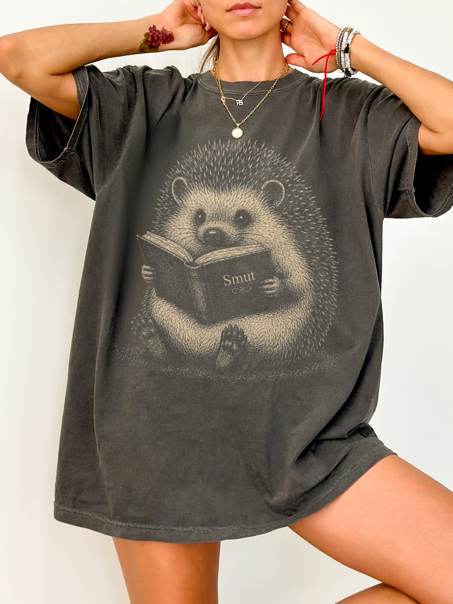 Woman wearing a pepper oversized t shirt with detailed hedgehog illustration reading a book labeled smut cozy book lover aesthetic graphic tee