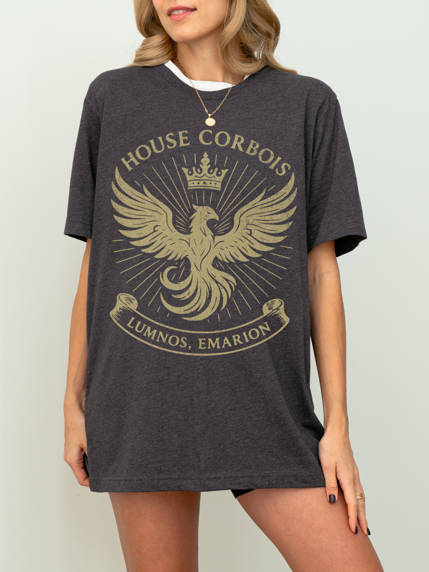 Model wearing a dark heather grey House Corbois t-shirt with a vintage golden phoenix crest and crown. A soft, oversized tee perfect for repping your favorite fantasy realm in everyday comfort.