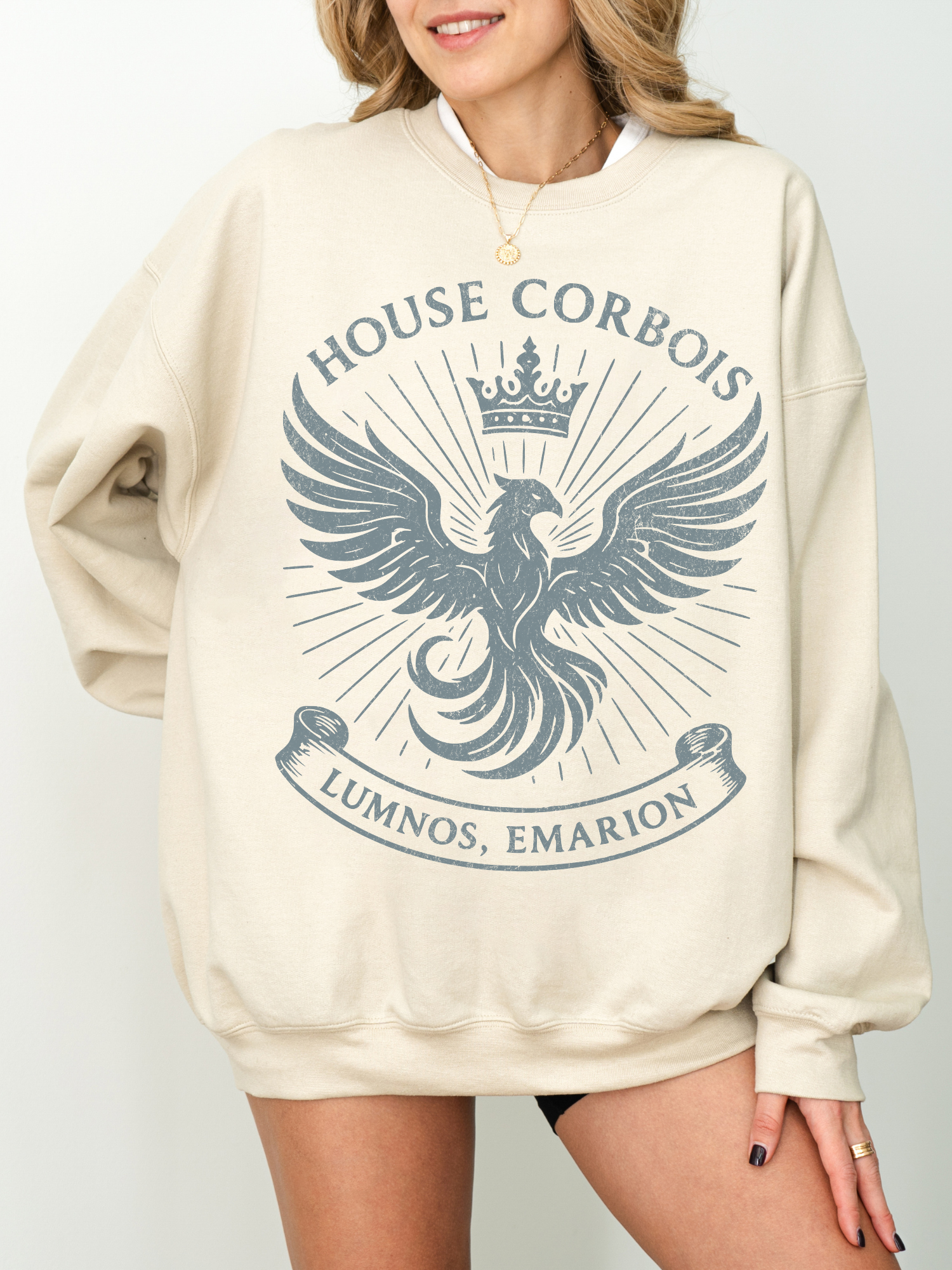 Woman smiling in neutral sand fantasy sweatshirt with dark blue vintage-style House Corbois graphic