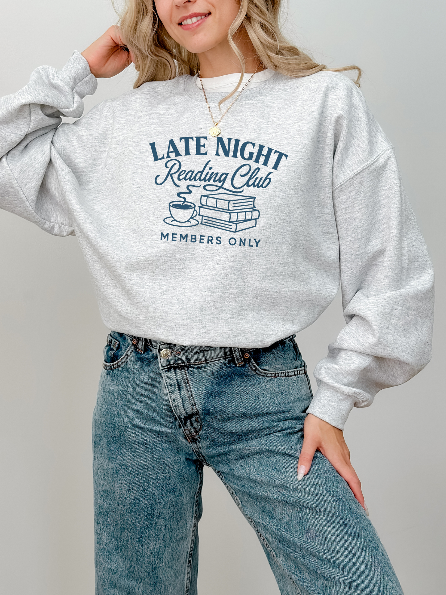 woman in am ash grey sweatshirt with navy text that says late night reading club members only and a line art coffee and books design
