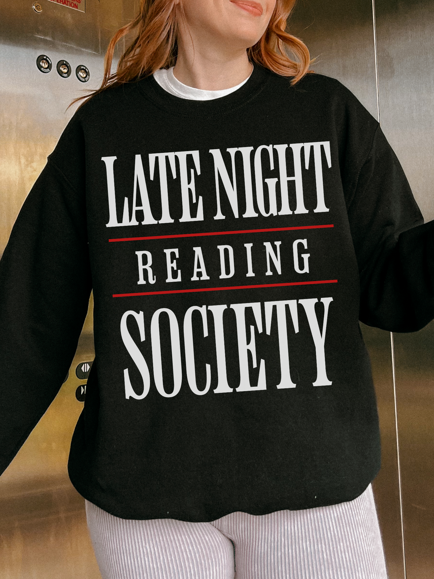 woman in an elevator wearing a black sweatshirt that says late night reading society in white with red lines