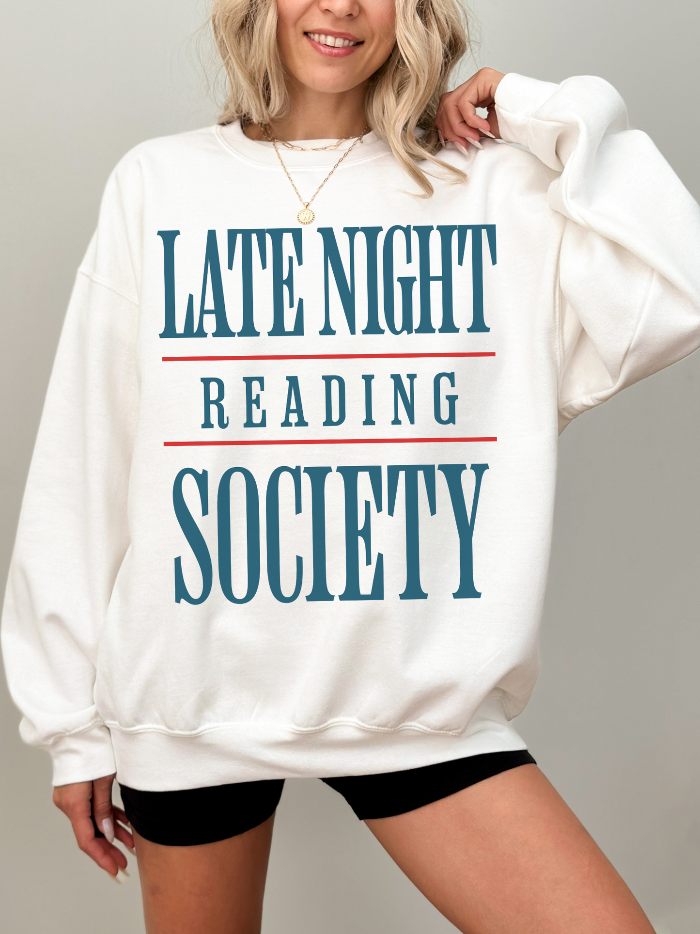 woman wearing a white sweatshirt with bold blue and red text that says late night reading society