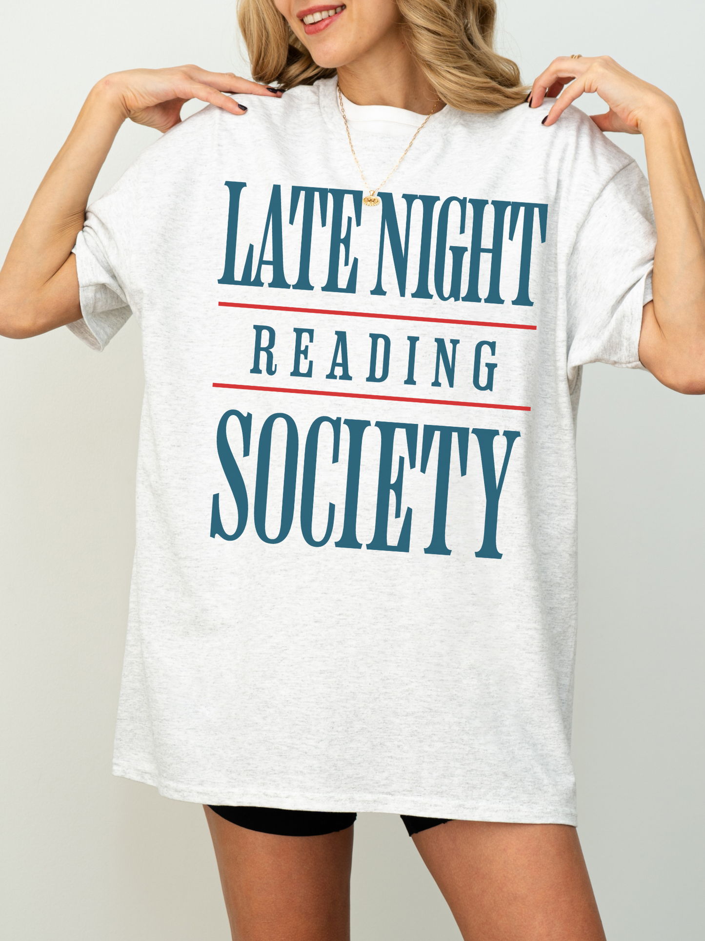 woman wearing an ash grey t-shirt that says late night reading society in bold blue and red graphic font