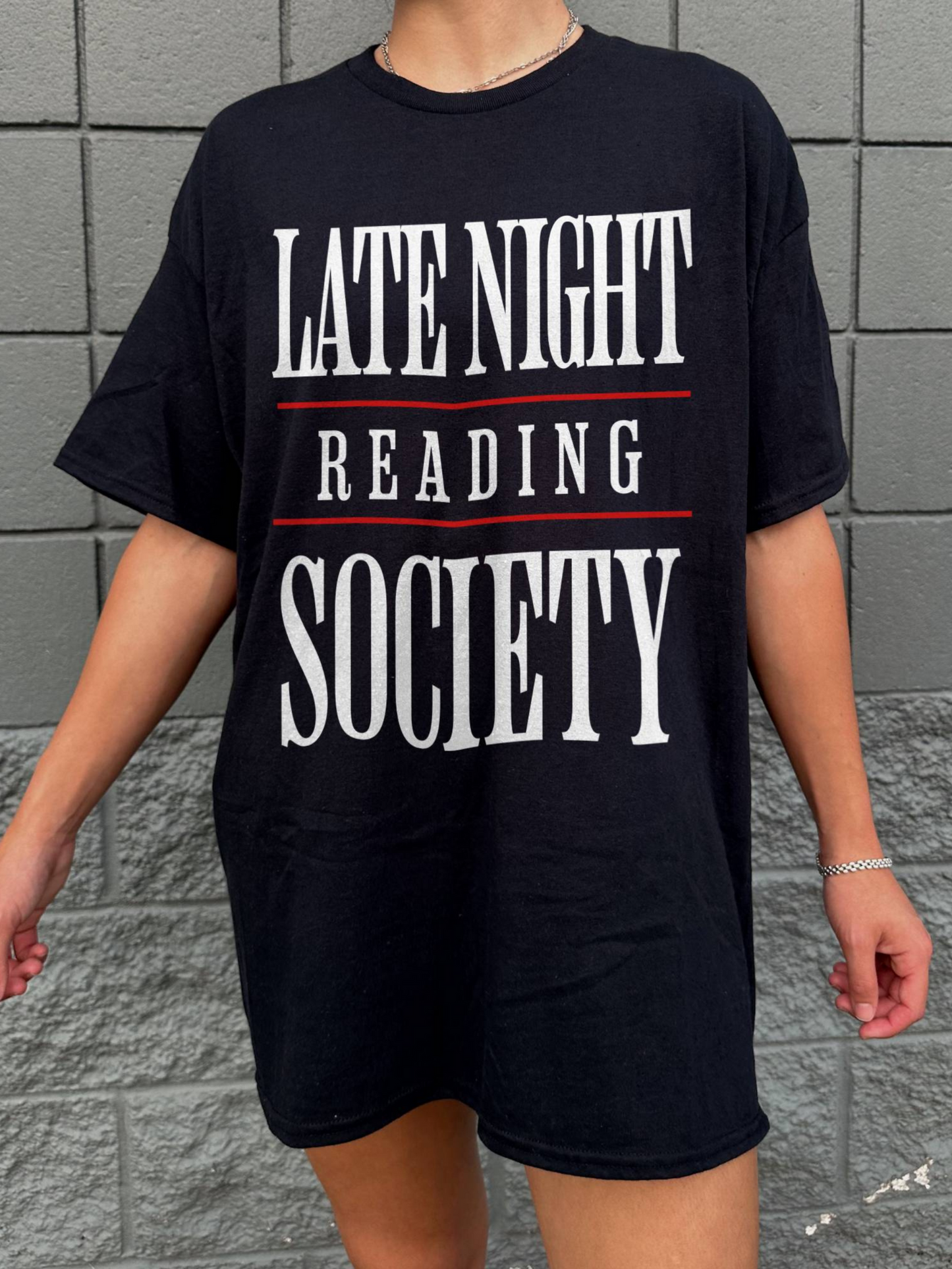 person wearing a black oversized t-shirt that says late night reading society in white text with red lines