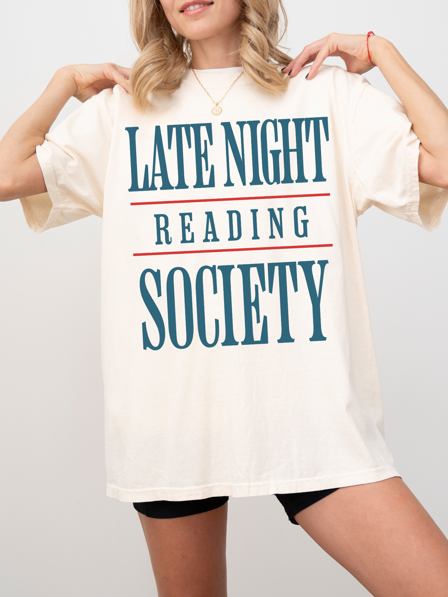 woman wearing a natural t-shirt that says late night reading society in teal blue text with red accent lines