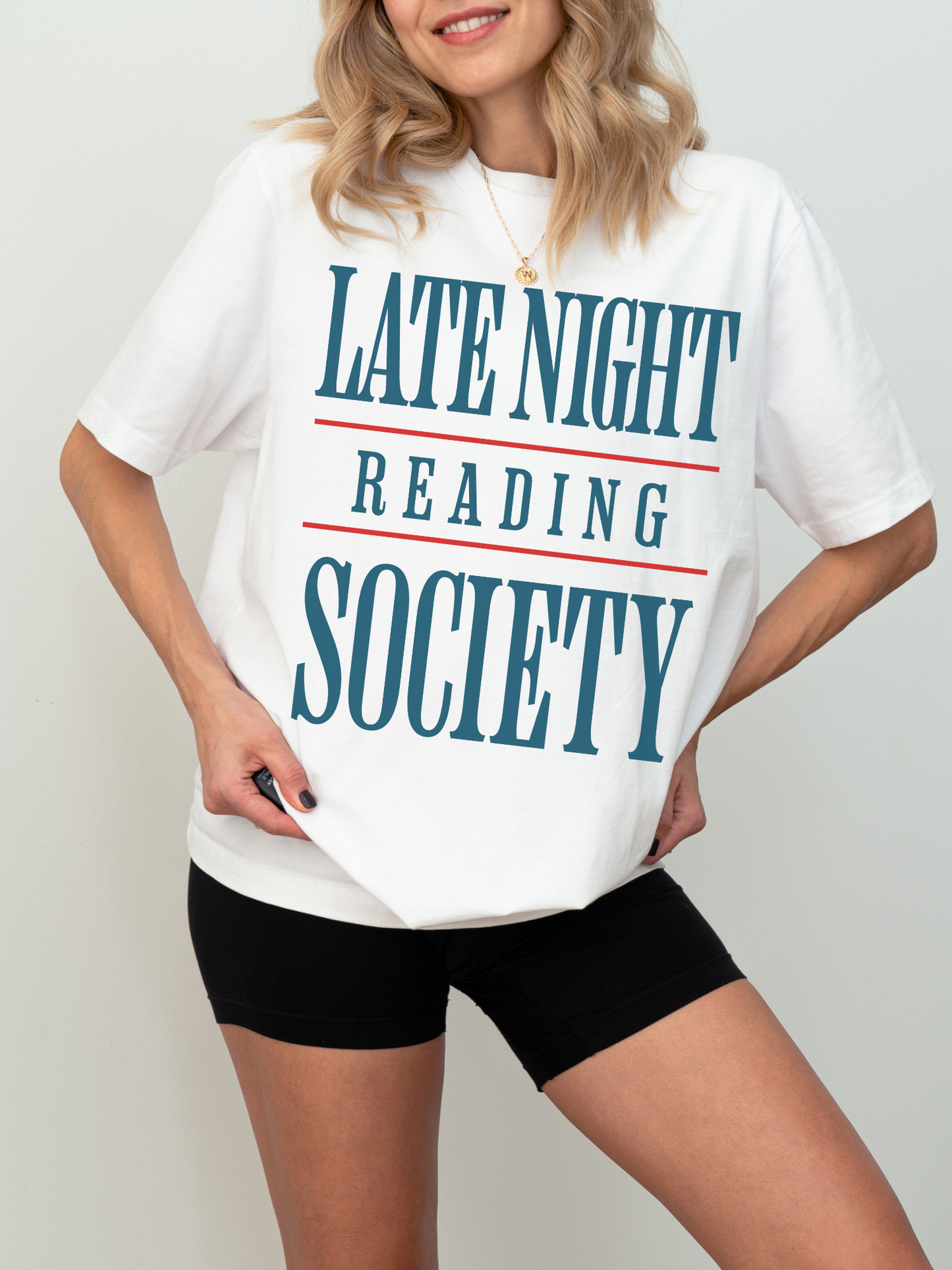 woman wearing a white t-shirt that says late night reading society in teal text with red lines above and below
