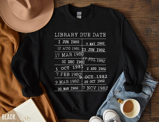 flat lay of black sweatshirt with library due date design, styled with coffee, book, and cozy outfit