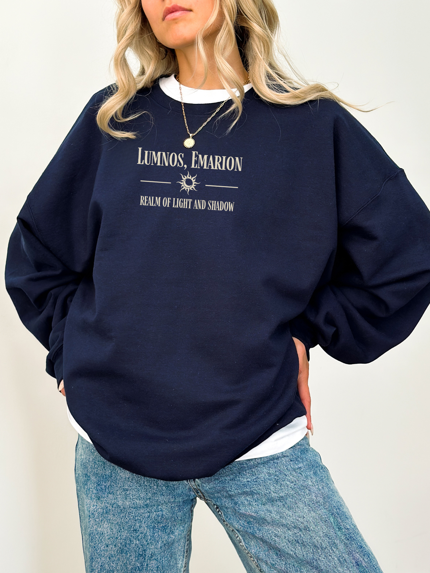 Woman wearing a navy Gildan sweatshirt with fantasy quote “Lumnos, Emarion,” styled with a layered white shirt and blue jeans.