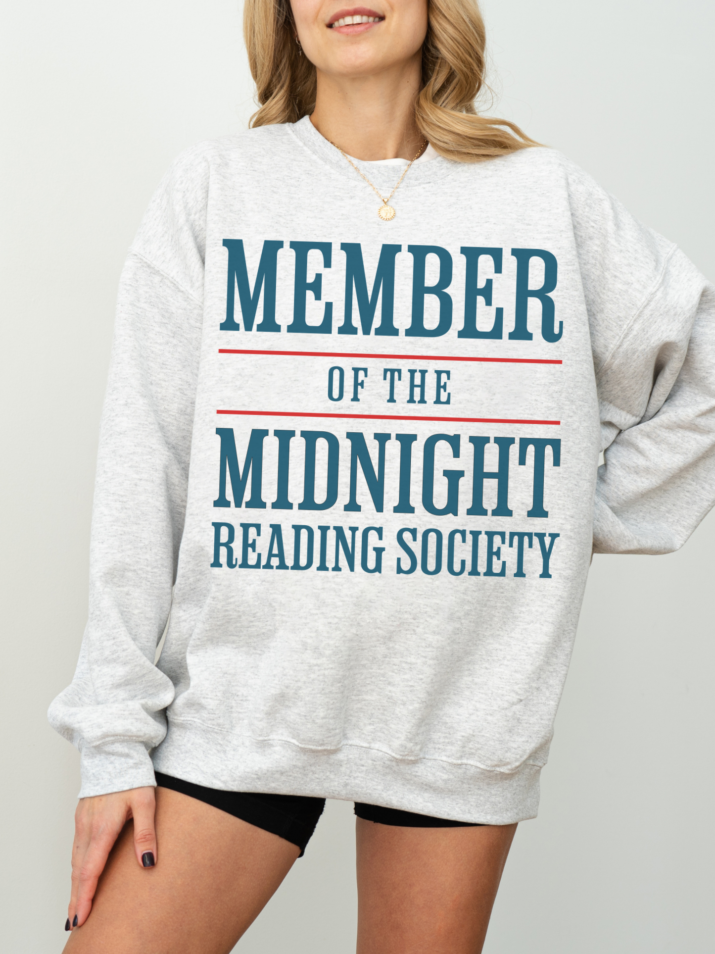 woman wearing an ash grey sweatshirt with large blue and red text that says member of the midnight reading society