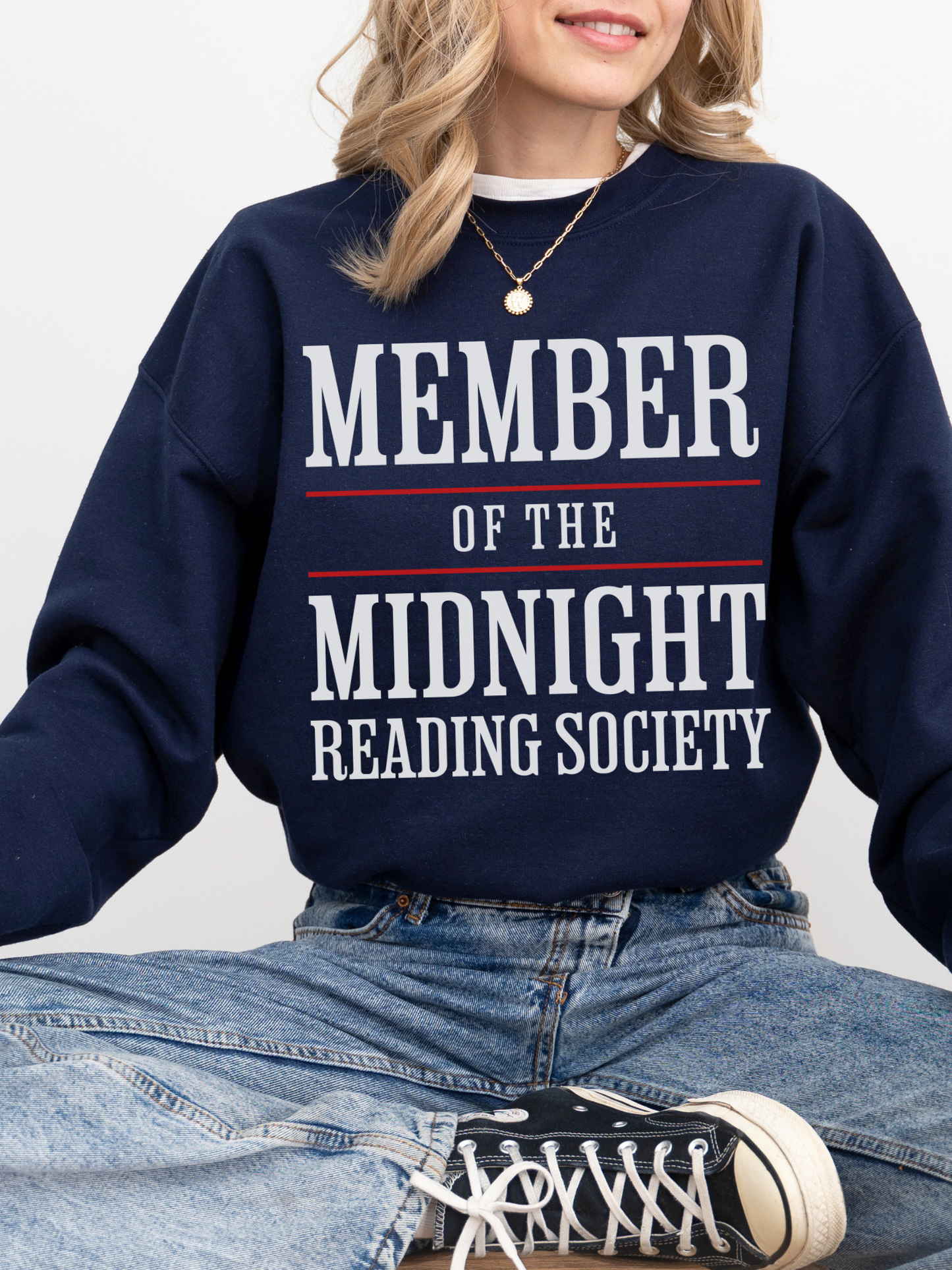 woman sitting in a navy sweatshirt with large white and red text that says member of the midnight reading society