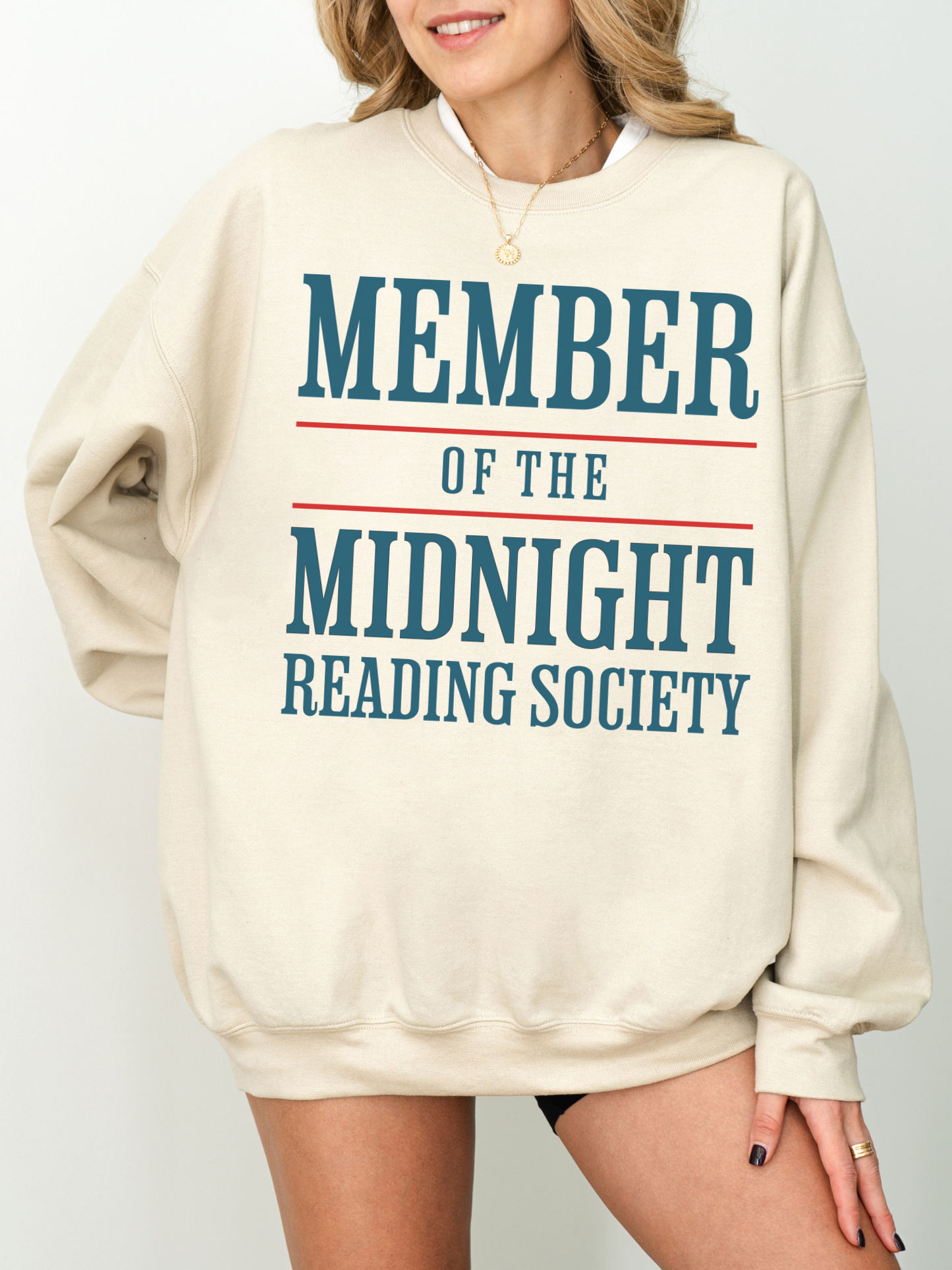 woman wearing a sand crewneck sweatshirt with bold teal and red typography reading member of the midnight reading society