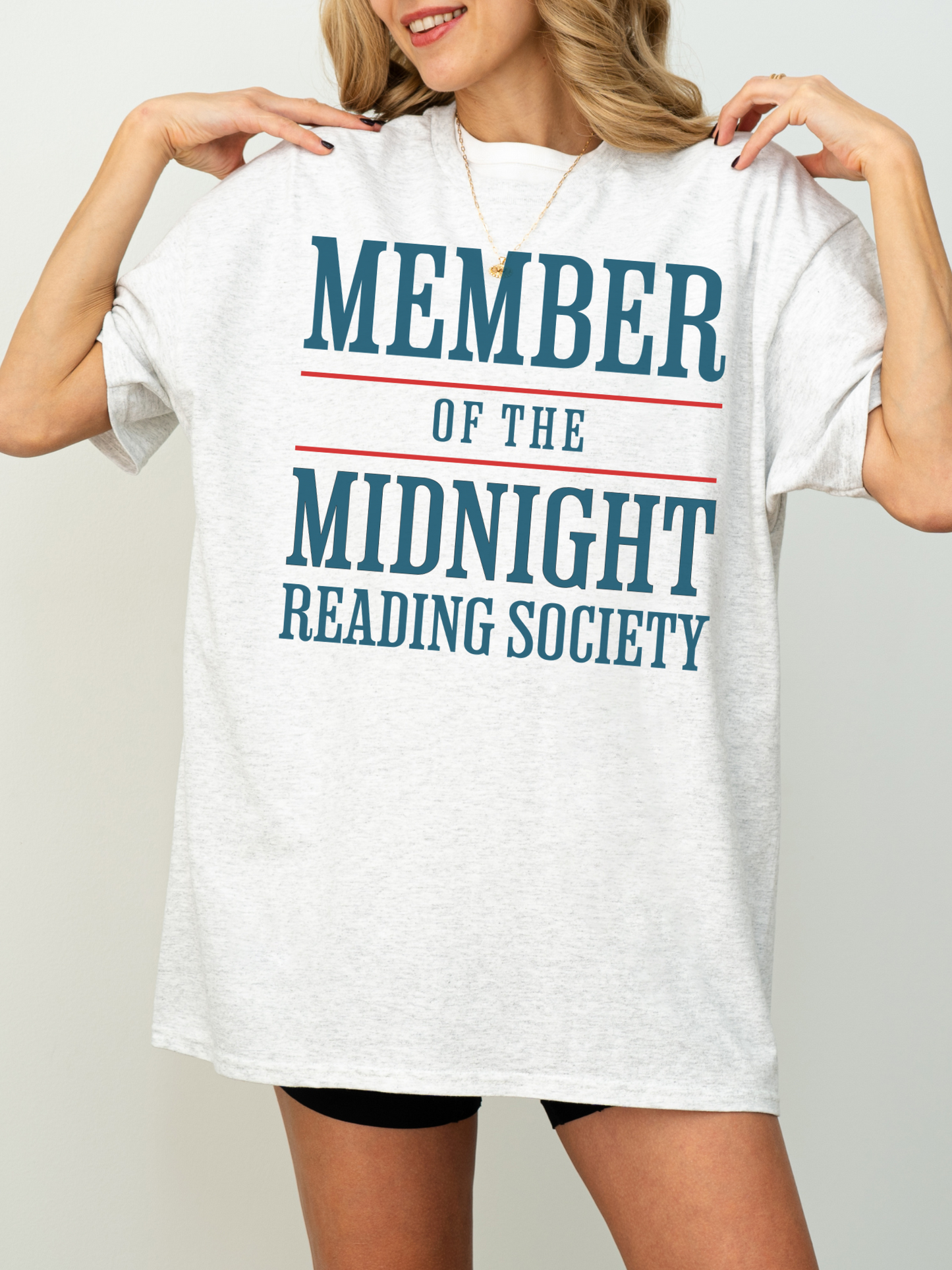 woman wearing an ash grey t-shirt with bold teal and red text that says member of the midnight reading society