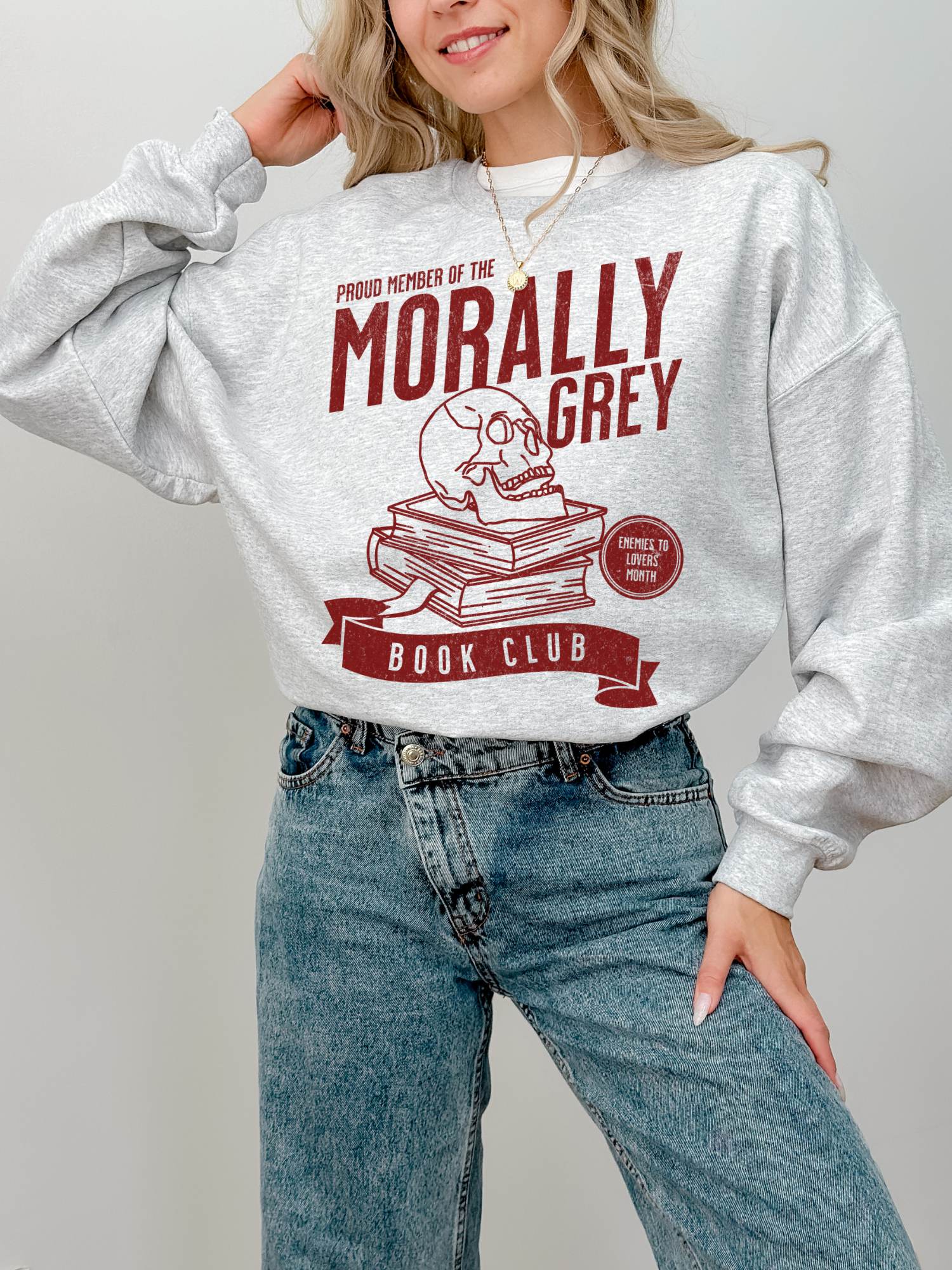 woman wearing ash grey sweatshirt with red morally grey book club design featuring skull and stacked books